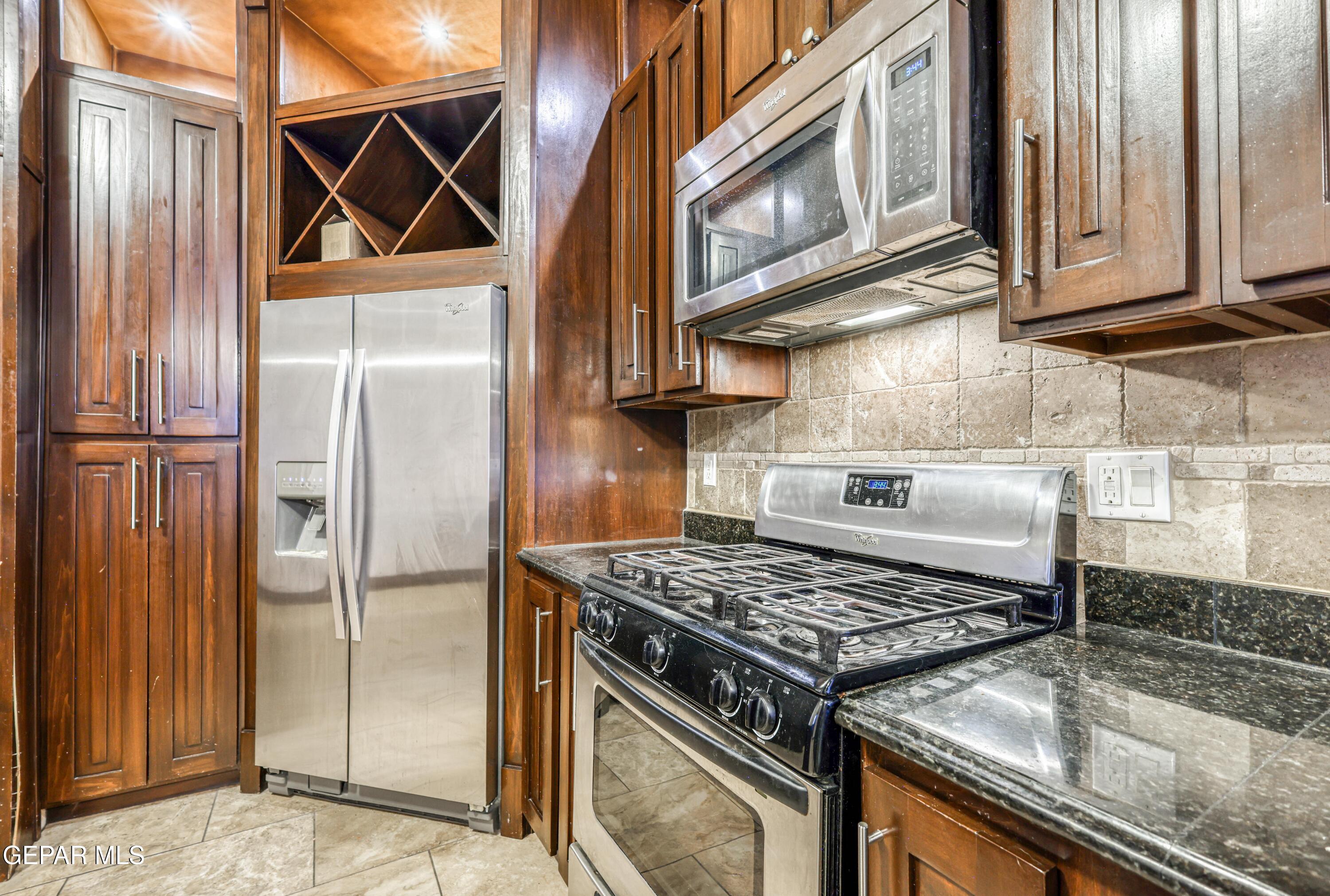 Kitchen with dark wood cabinets, stainless-steel appliances, and beige stone tile backsplash.