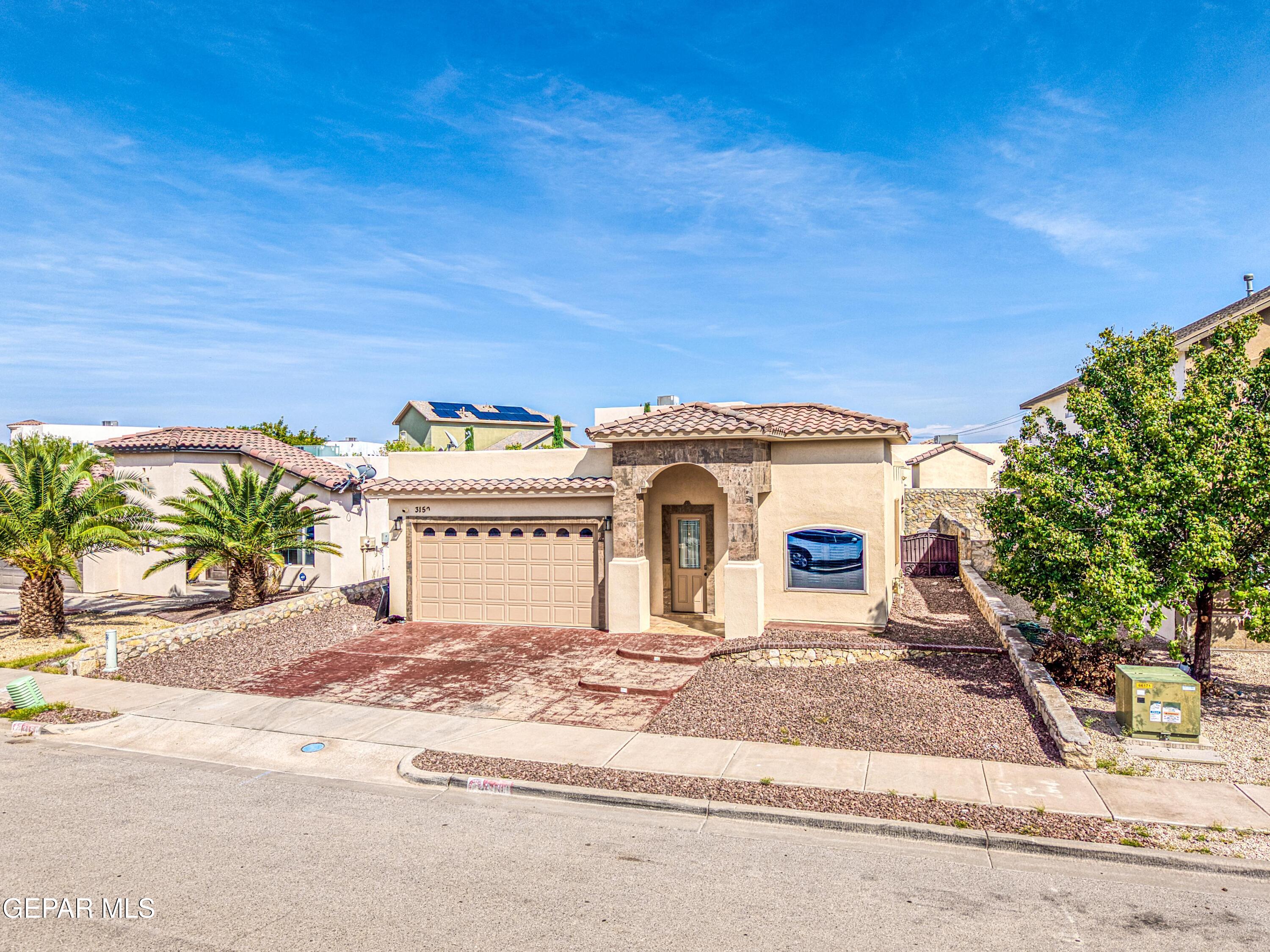 Single-story stucco home with a tile roof, stone-trimmed arched entry, and gravel landscaping.