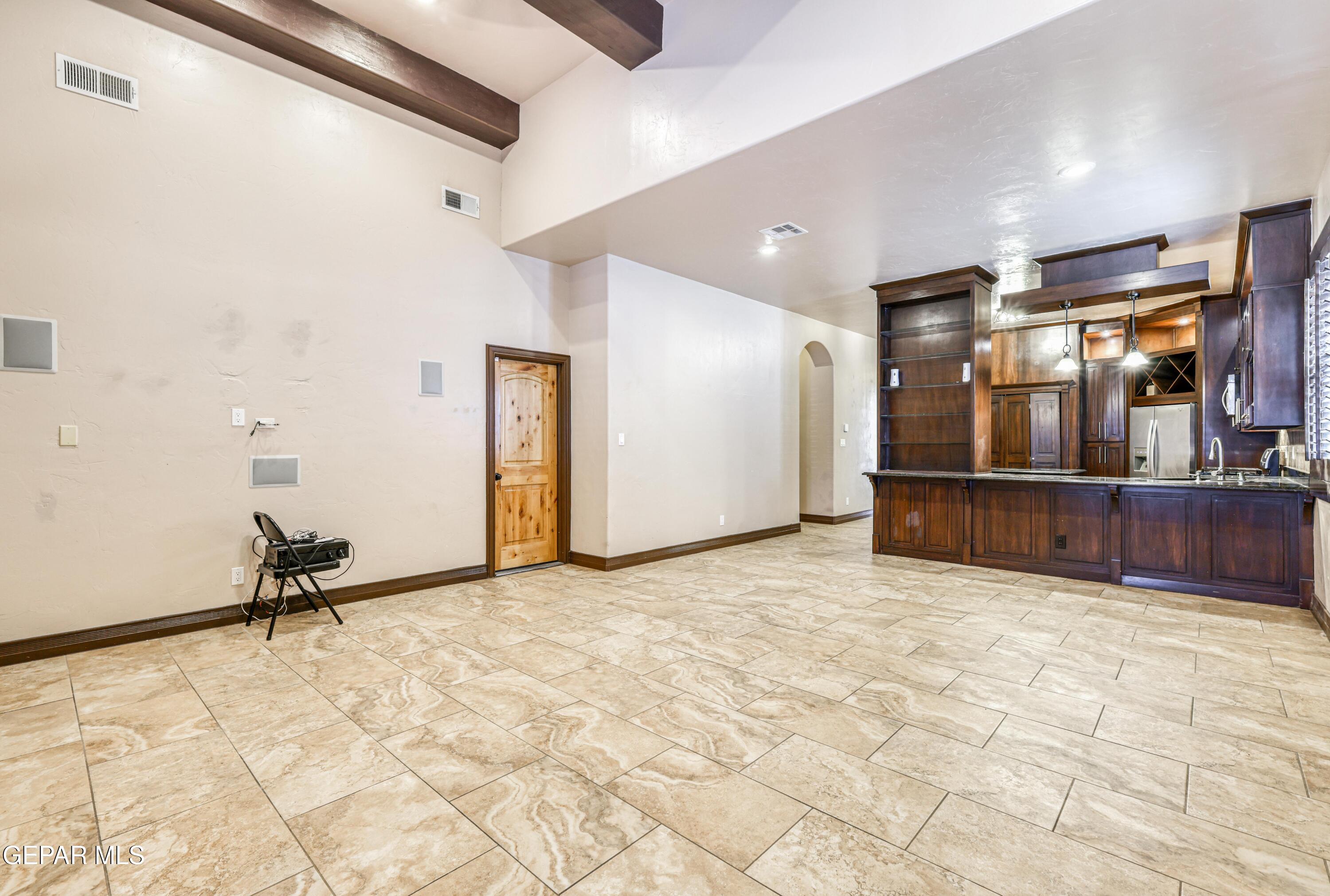 Open-plan kitchen and living area with dark wood cabinetry, tiled floors, and exposed ceiling beams.