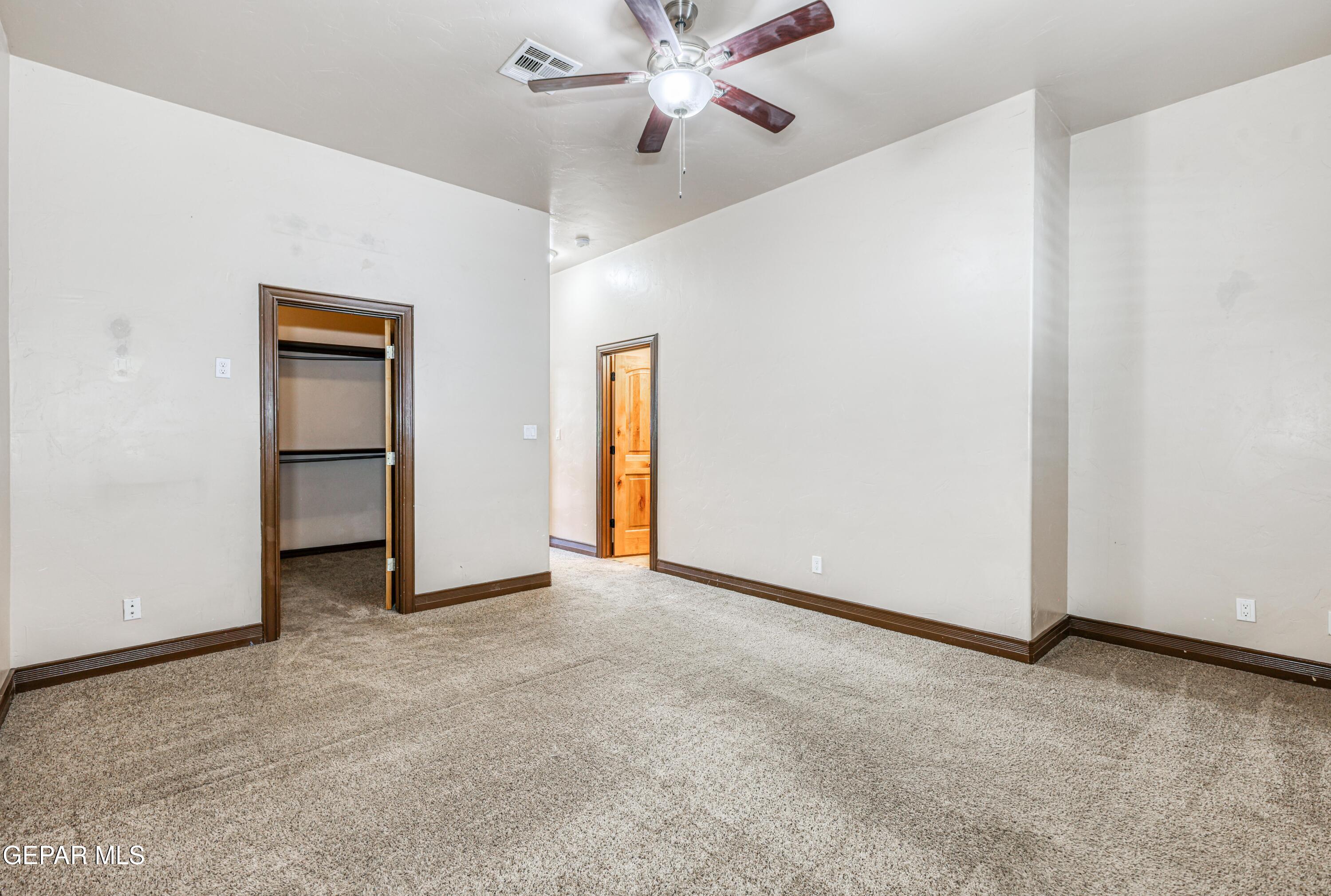 Empty carpeted bedroom with an open closet and ceiling fan.