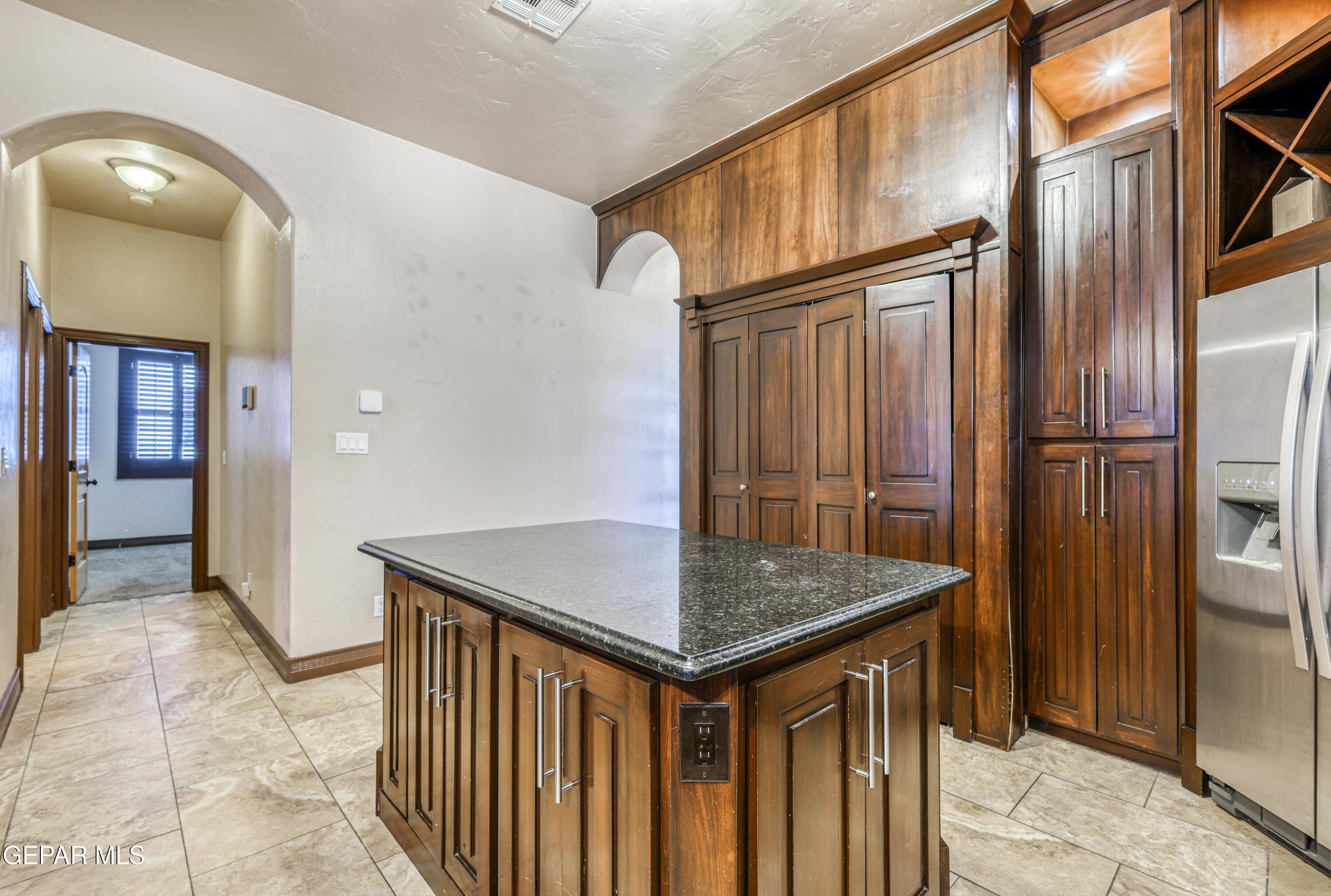 Kitchen with dark wood cabinets, a granite-topped island, and a stainless steel refrigerator.