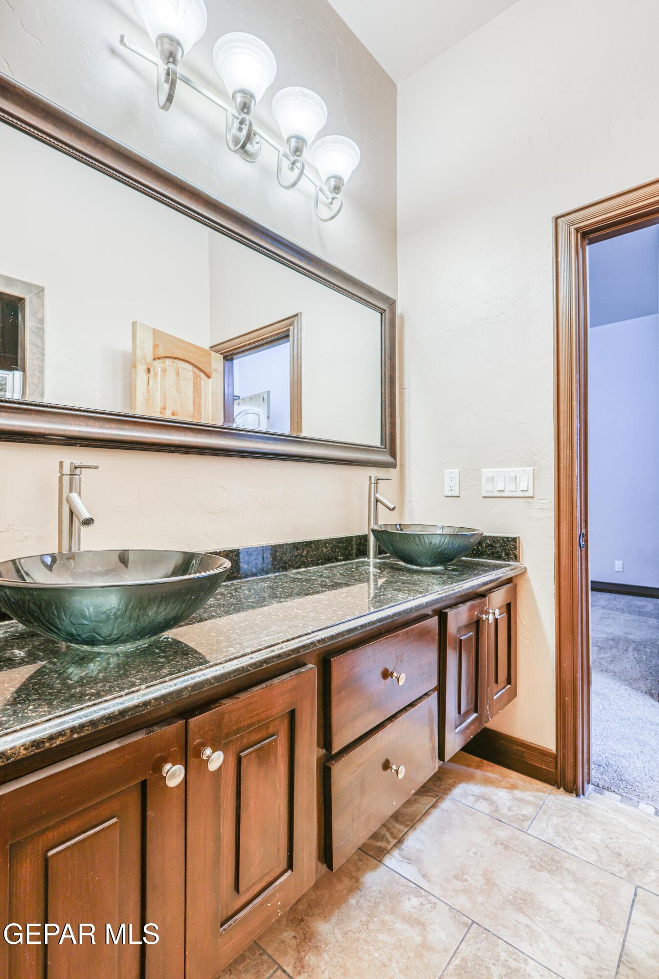 Bathroom vanity with two green vessel sinks, dark granite countertop, and rich wood cabinetry.