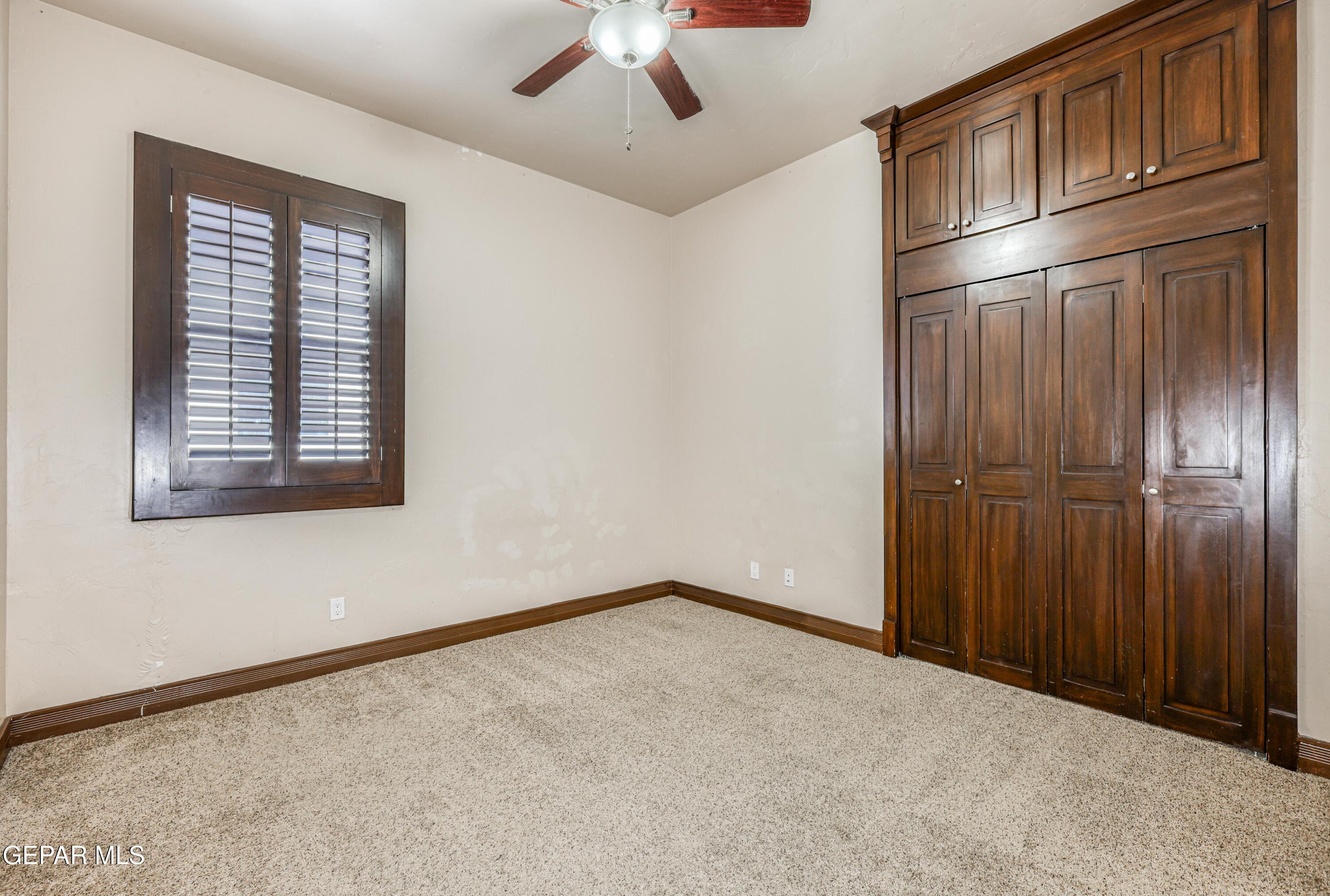 Empty bedroom with beige carpet, dark wood built-in wardrobes, and a shuttered window.