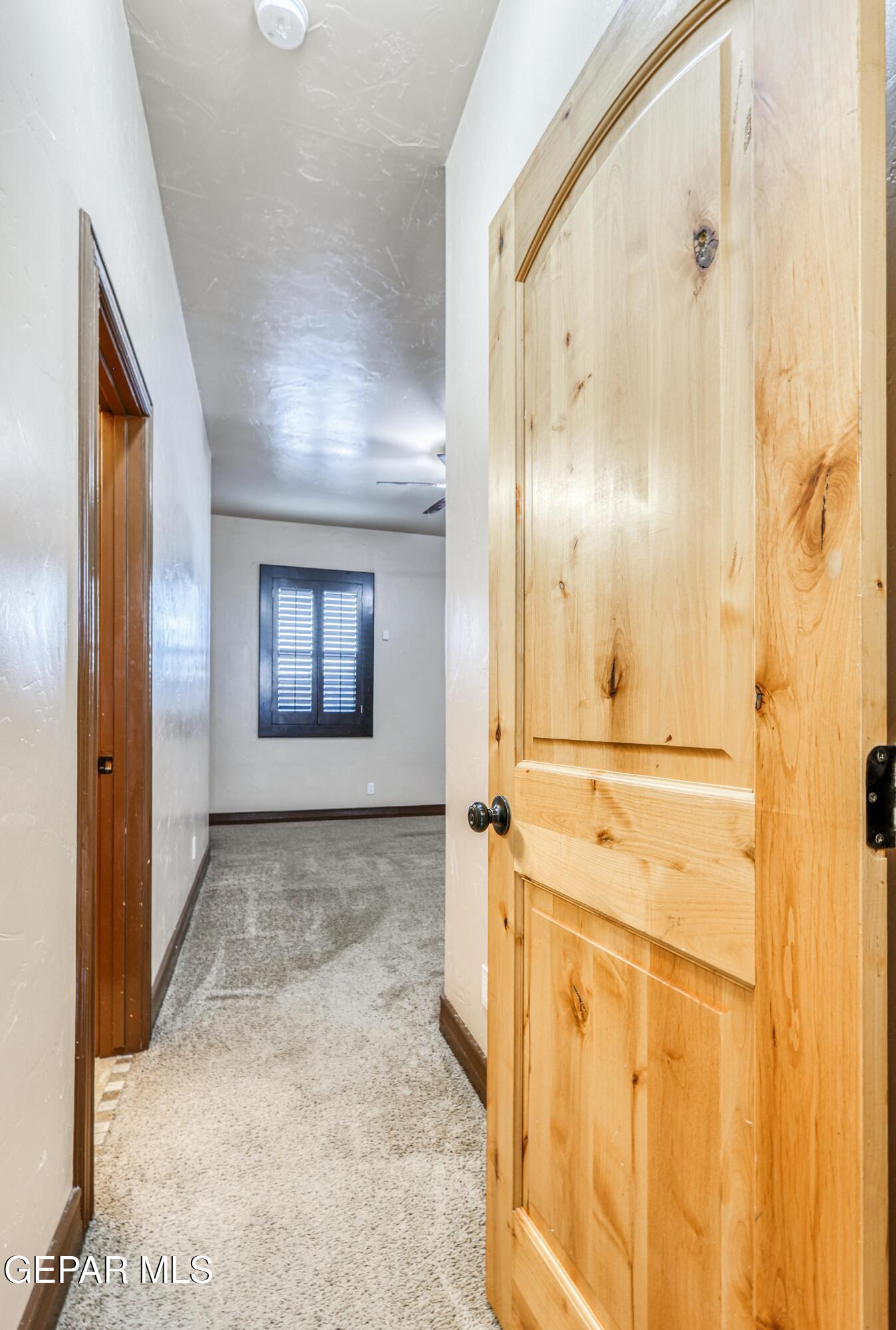 Hallway with carpet and a large open natural-wood door beside a shuttered window.