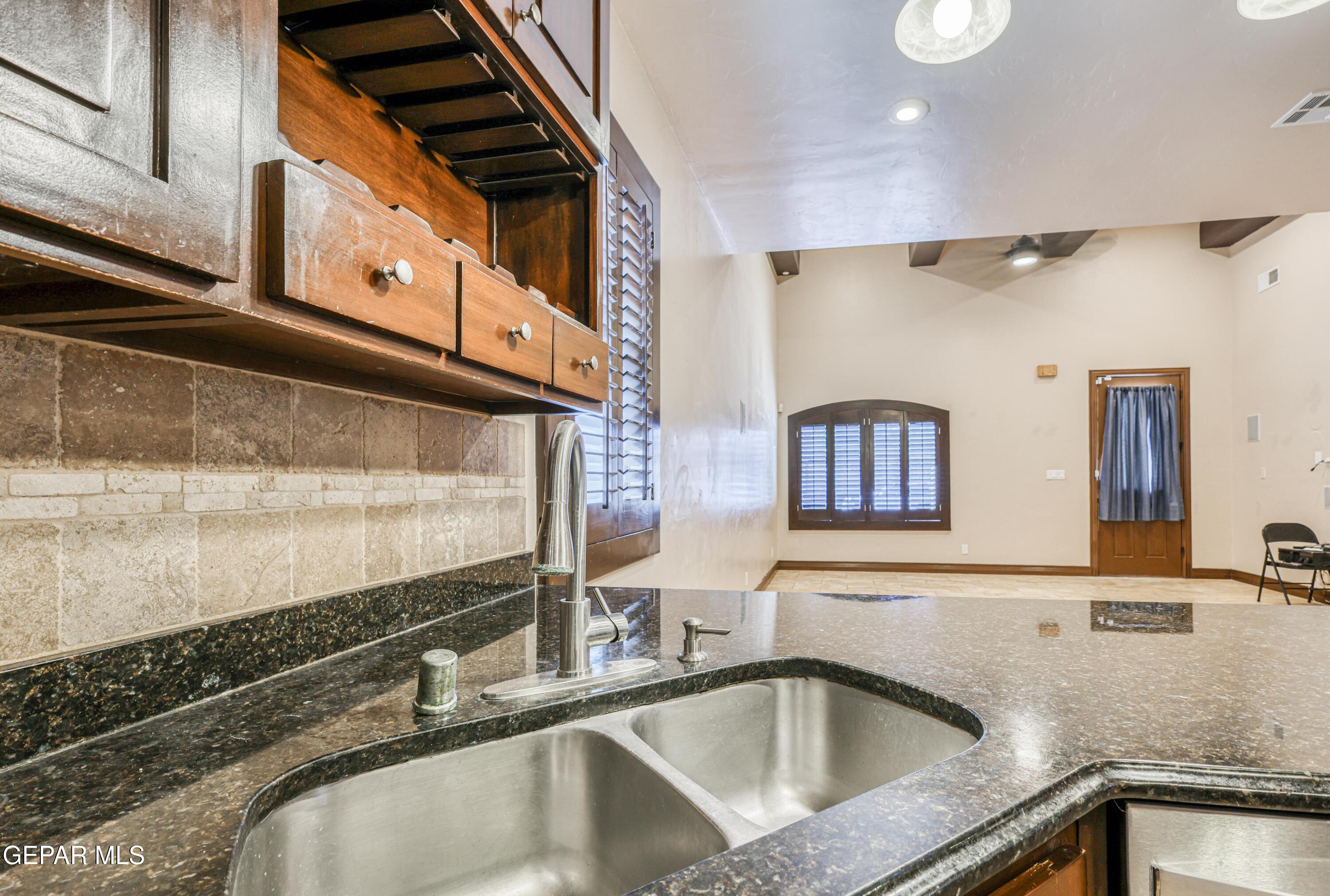 Kitchen with double-basin sink, dark granite counters, wood cabinets, and stone tile backsplash.