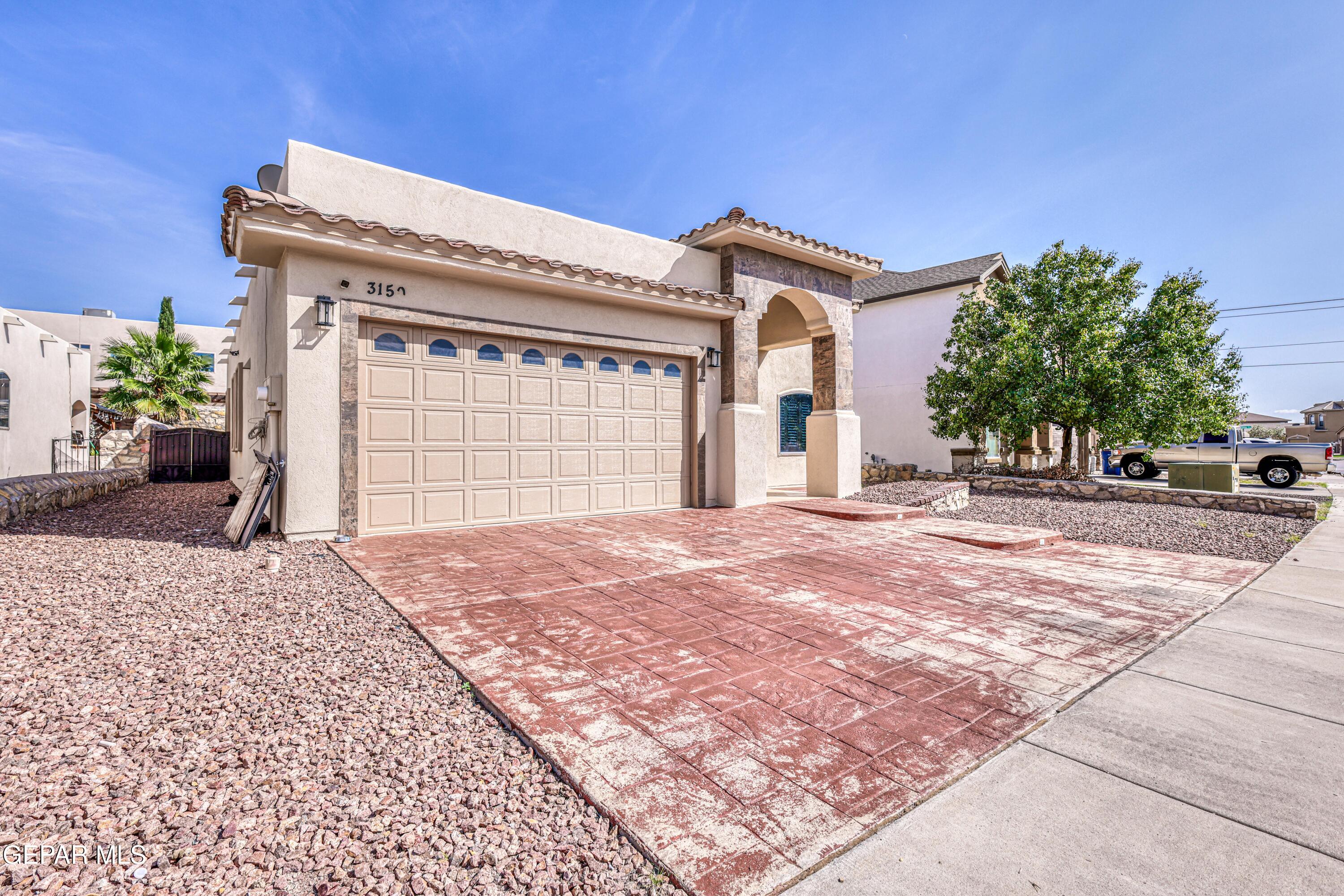 Stucco home with an arched entry, double garage, and broad red stamped-concrete driveway.