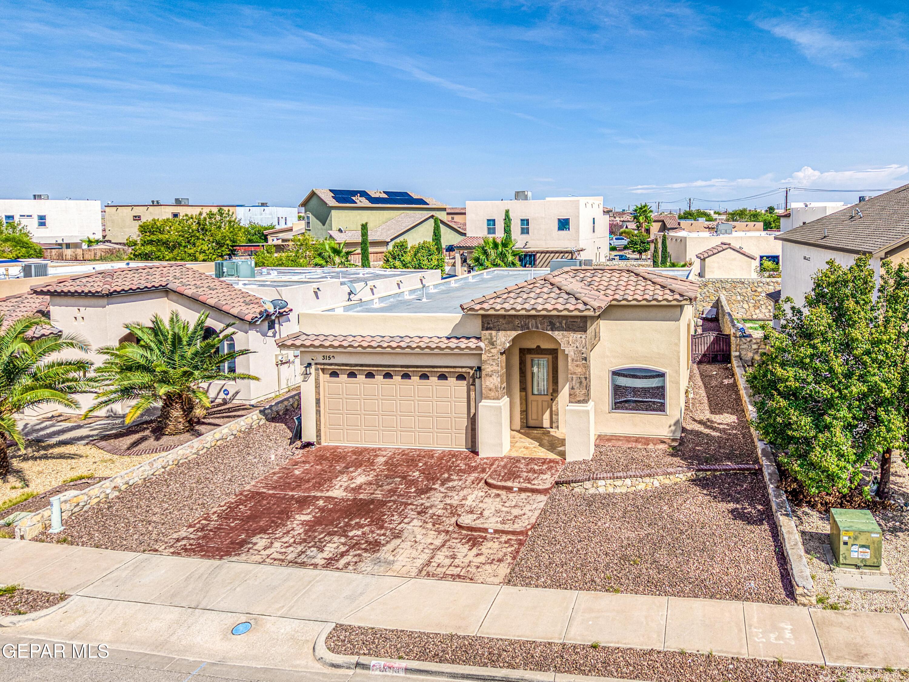 Tan stucco home with a stone-trimmed entry, two-car garage, and gravel landscaping.