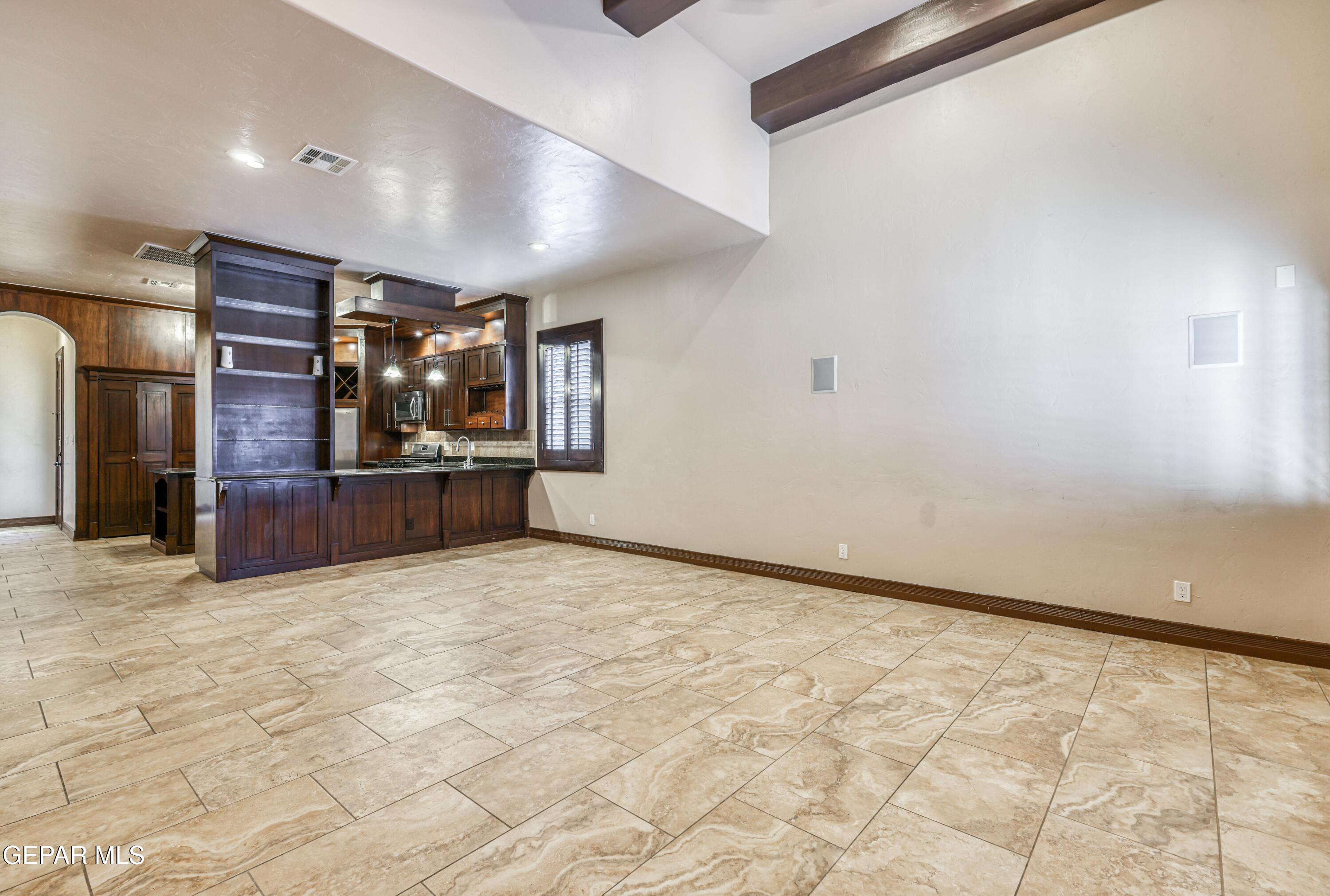 Unfurnished living area with stone tile floors, dark wood kitchen island and cabinetry, and exposed ceiling beam.
