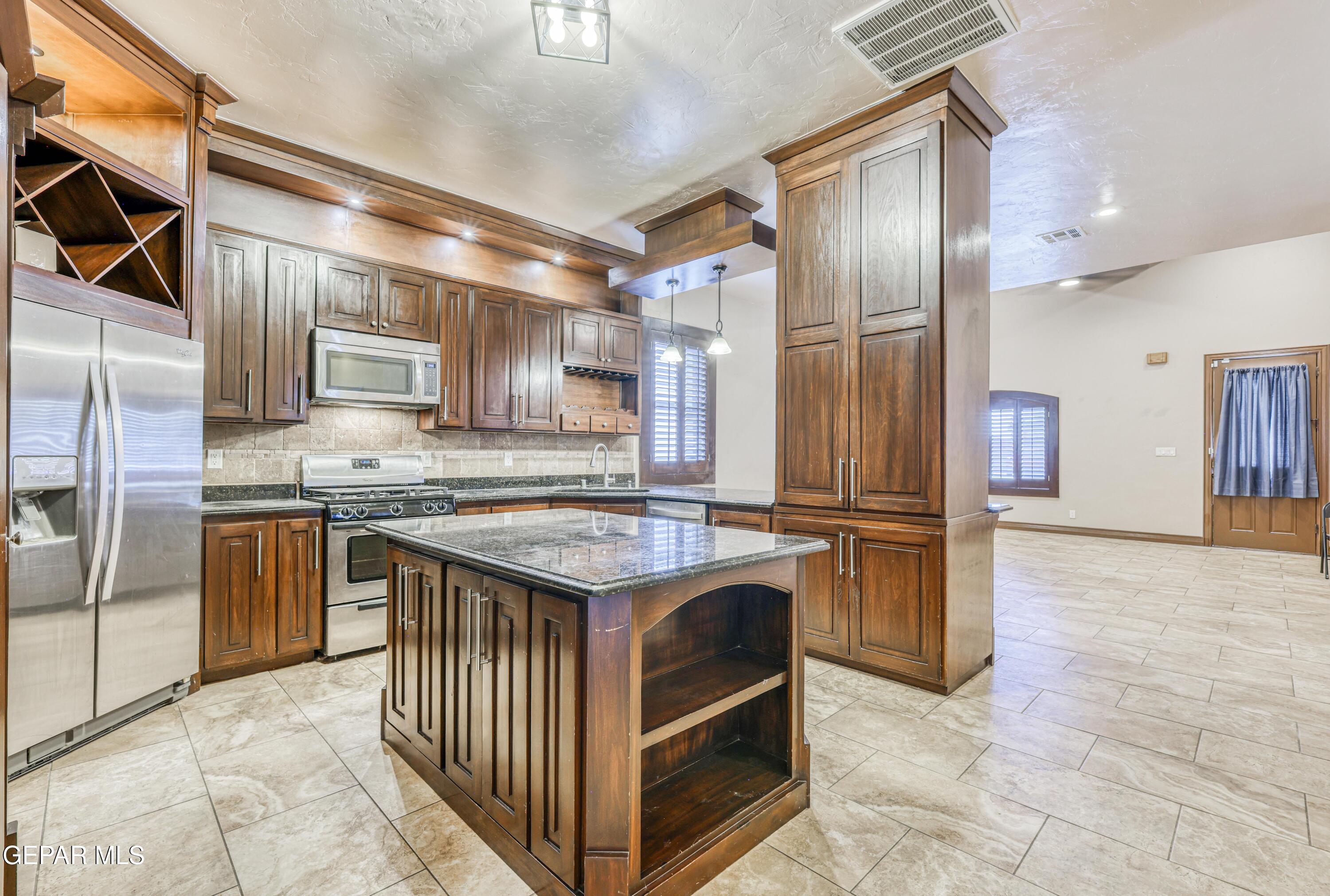 Kitchen with dark wood cabinets, stainless steel appliances, and a large island with open shelving.