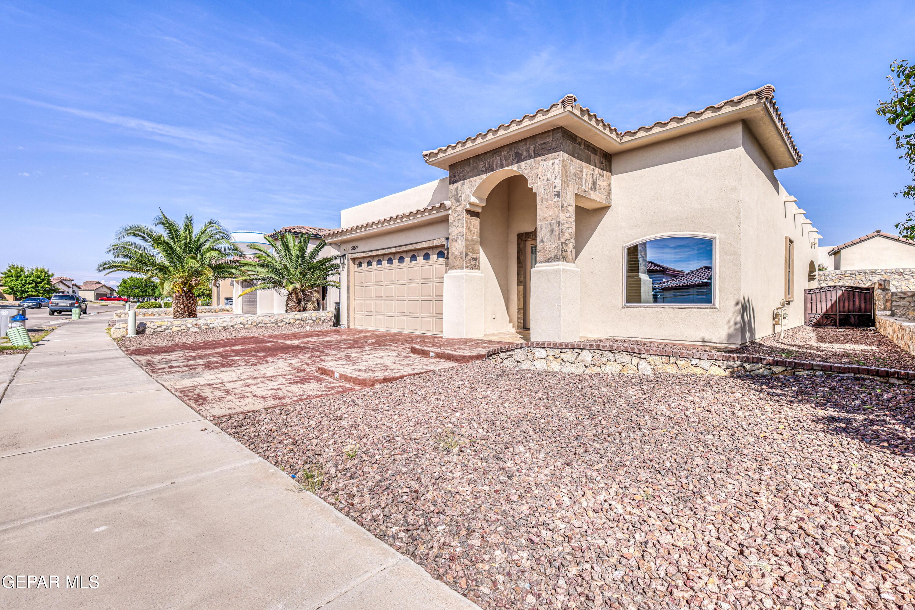 Stucco house with a stone-trimmed arched entry, tiled roof, two-car garage, and rock landscaping.