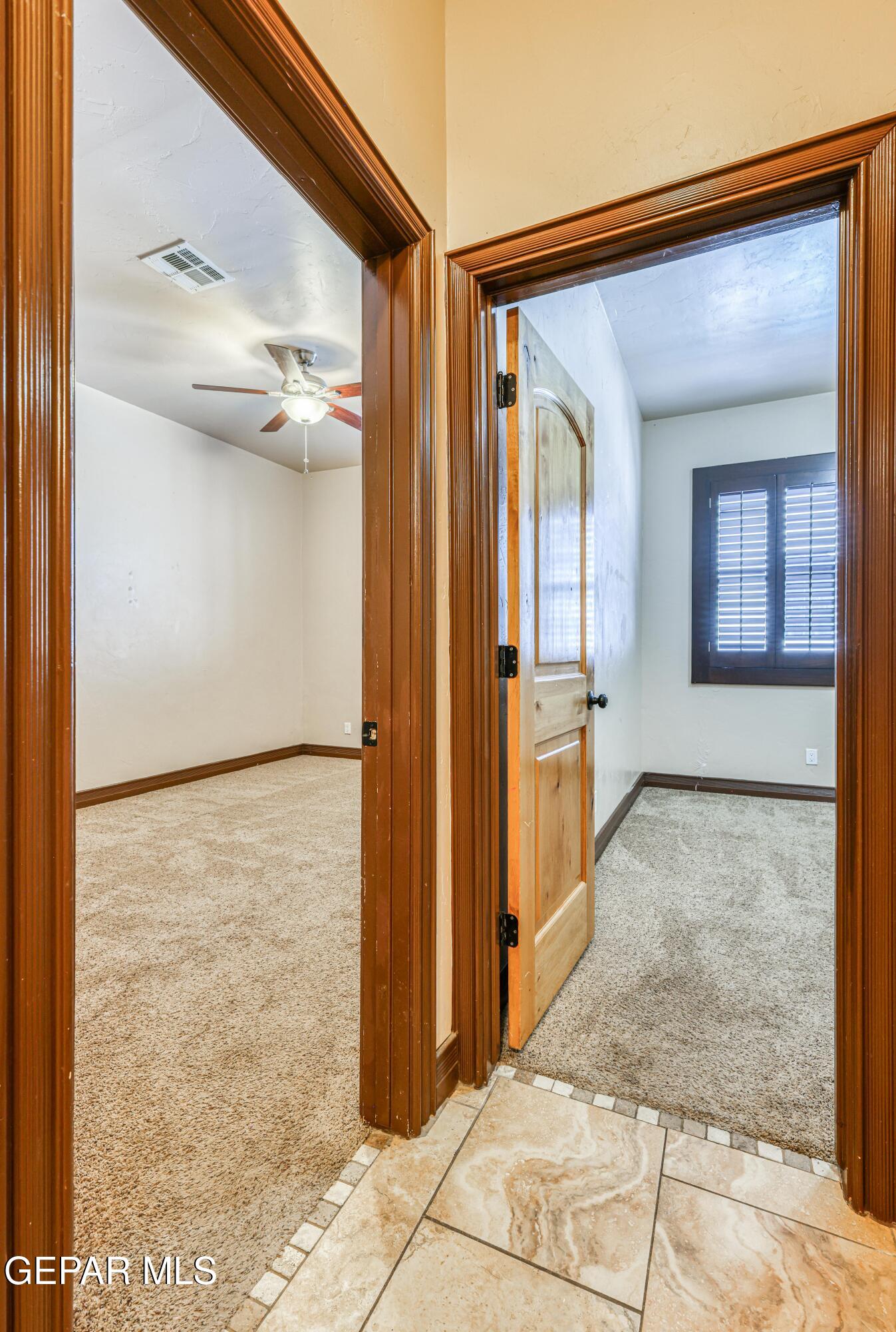 Two empty carpeted rooms with wood-trimmed doorways, a ceiling fan, and a shuttered window.