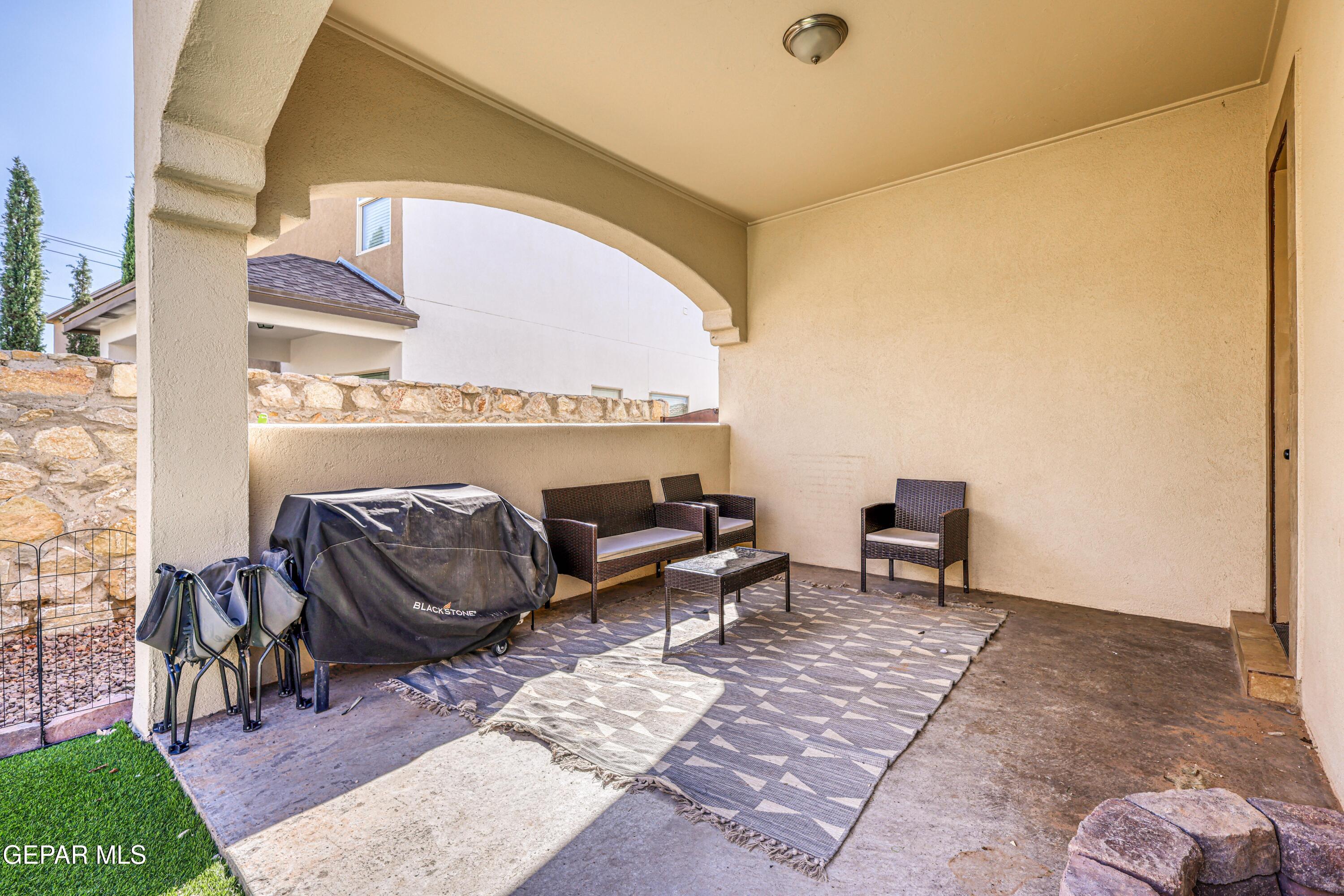 Covered patio with wicker seating, a patterned rug, and a covered grill.