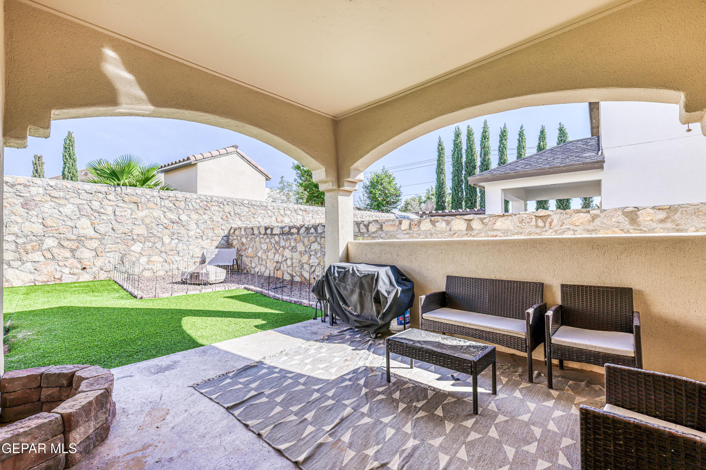 Covered patio with wicker seating and barbecue overlooking a stone-walled lawn.