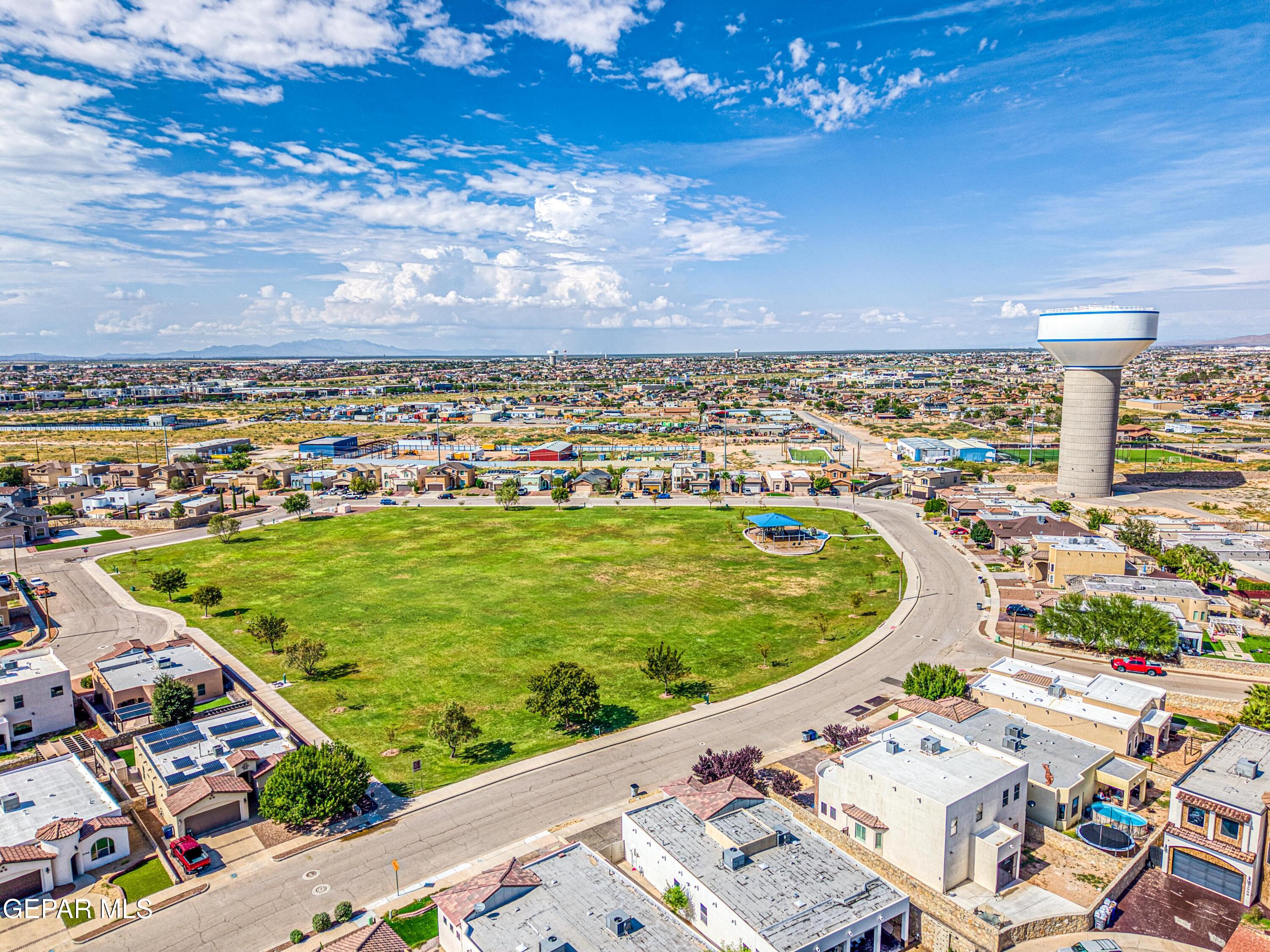 Aerial neighborhood view with a large oval park, water tower, and distant mountains.