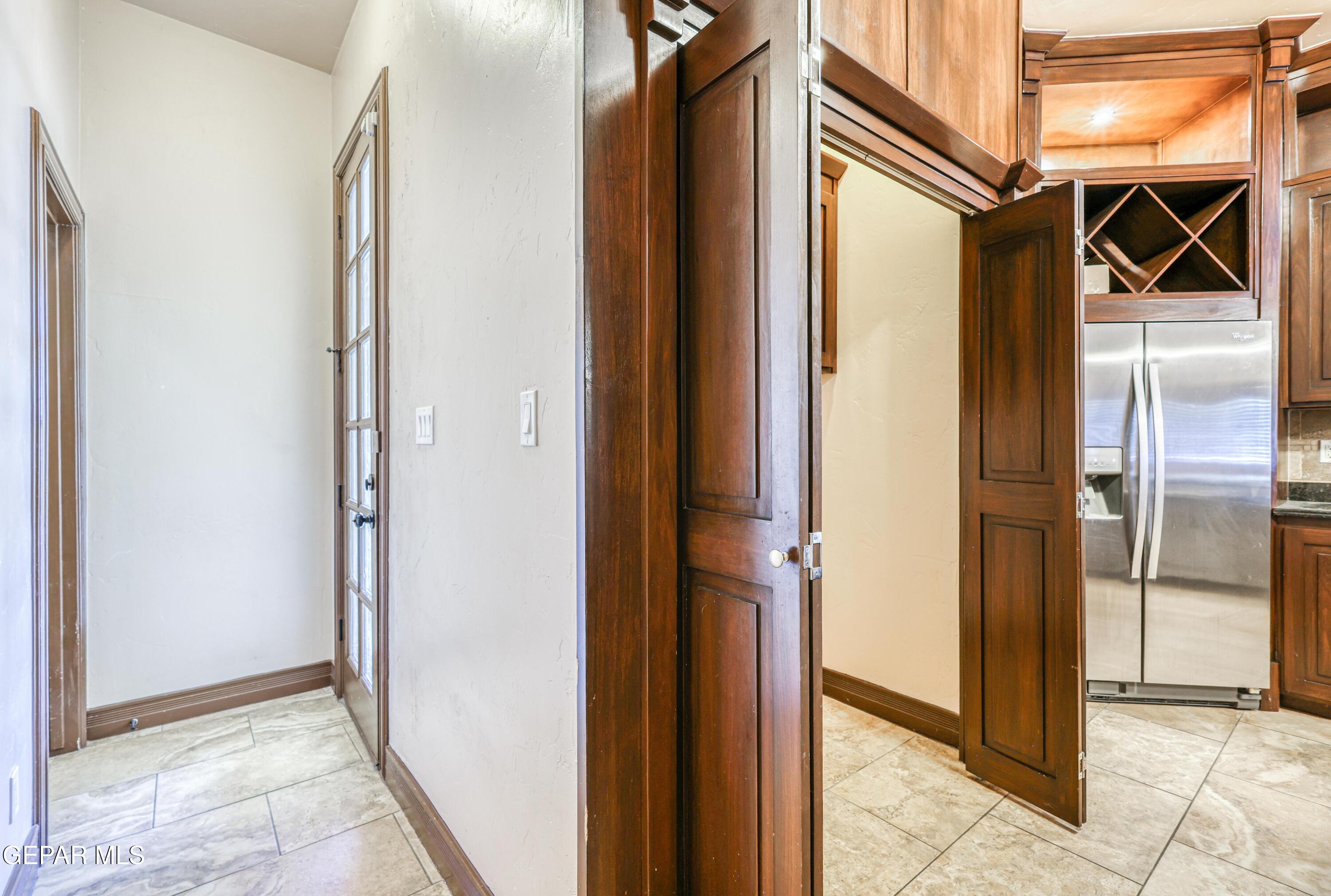 Tiled entry hall opening to a kitchen with dark wood cabinets, a built-in wine rack, and stainless steel refrigerator.