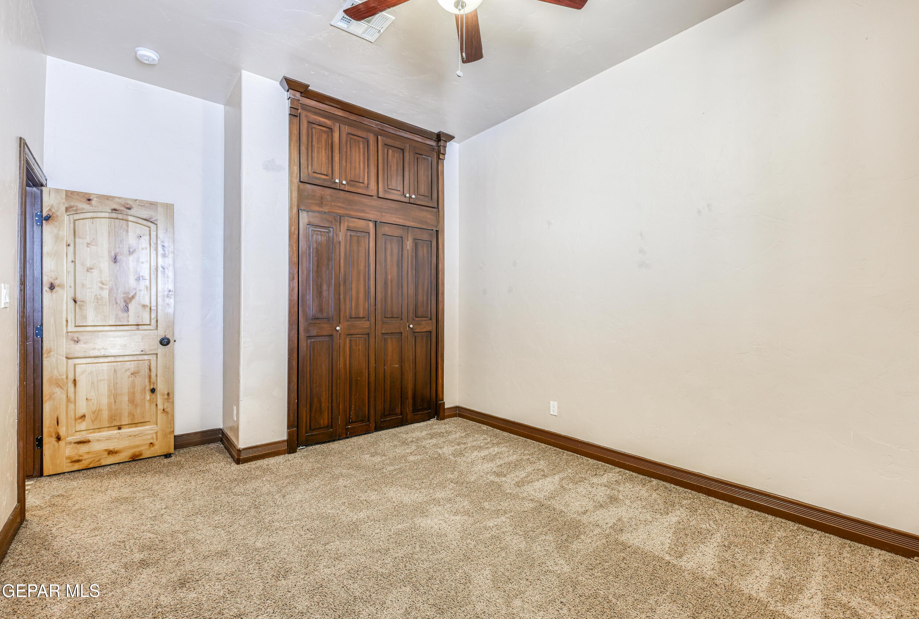 Empty bedroom with a tall dark wood built-in wardrobe and a light wood door.