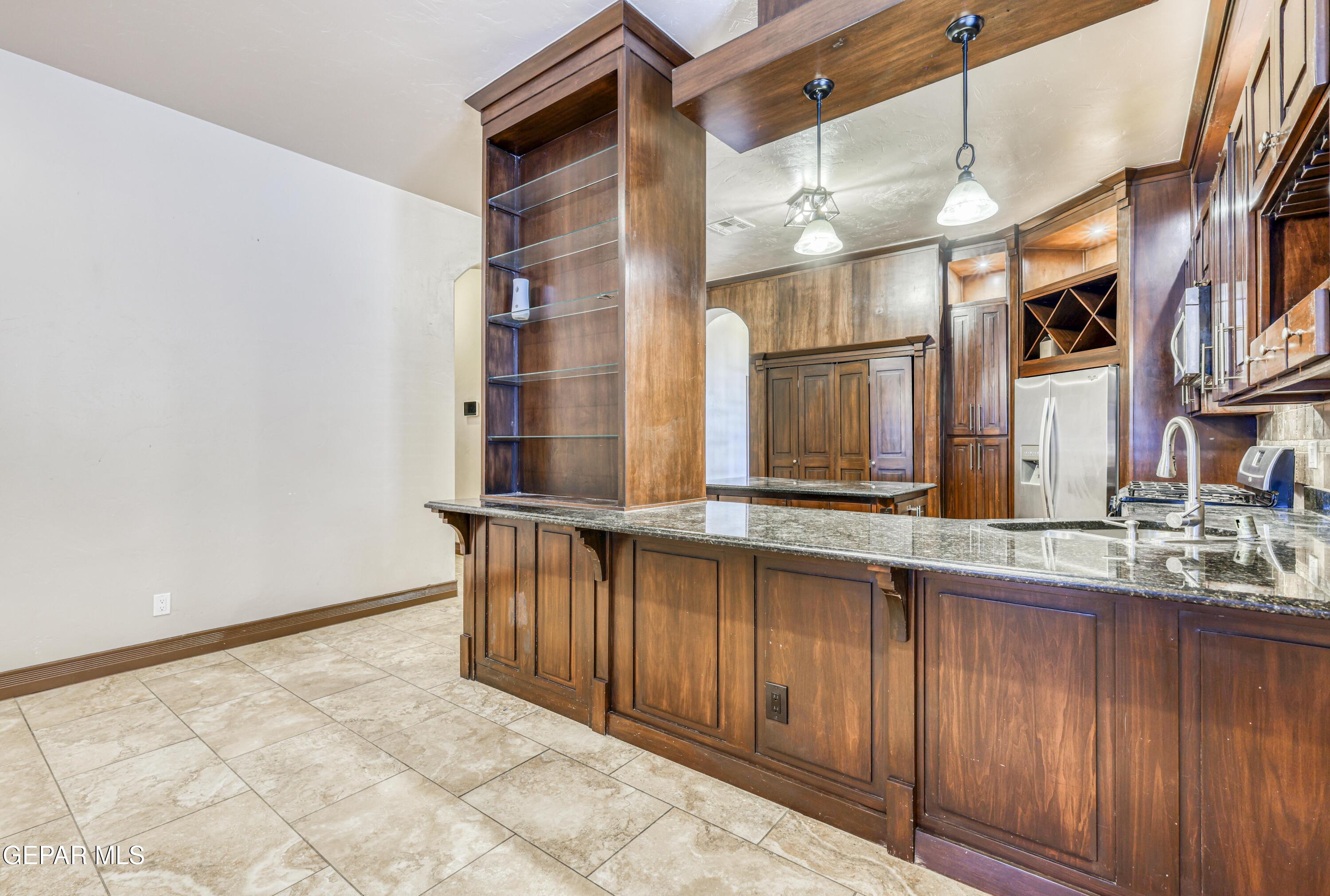 Kitchen with dark wood cabinetry, granite breakfast bar, glass shelving, and stainless steel appliances.