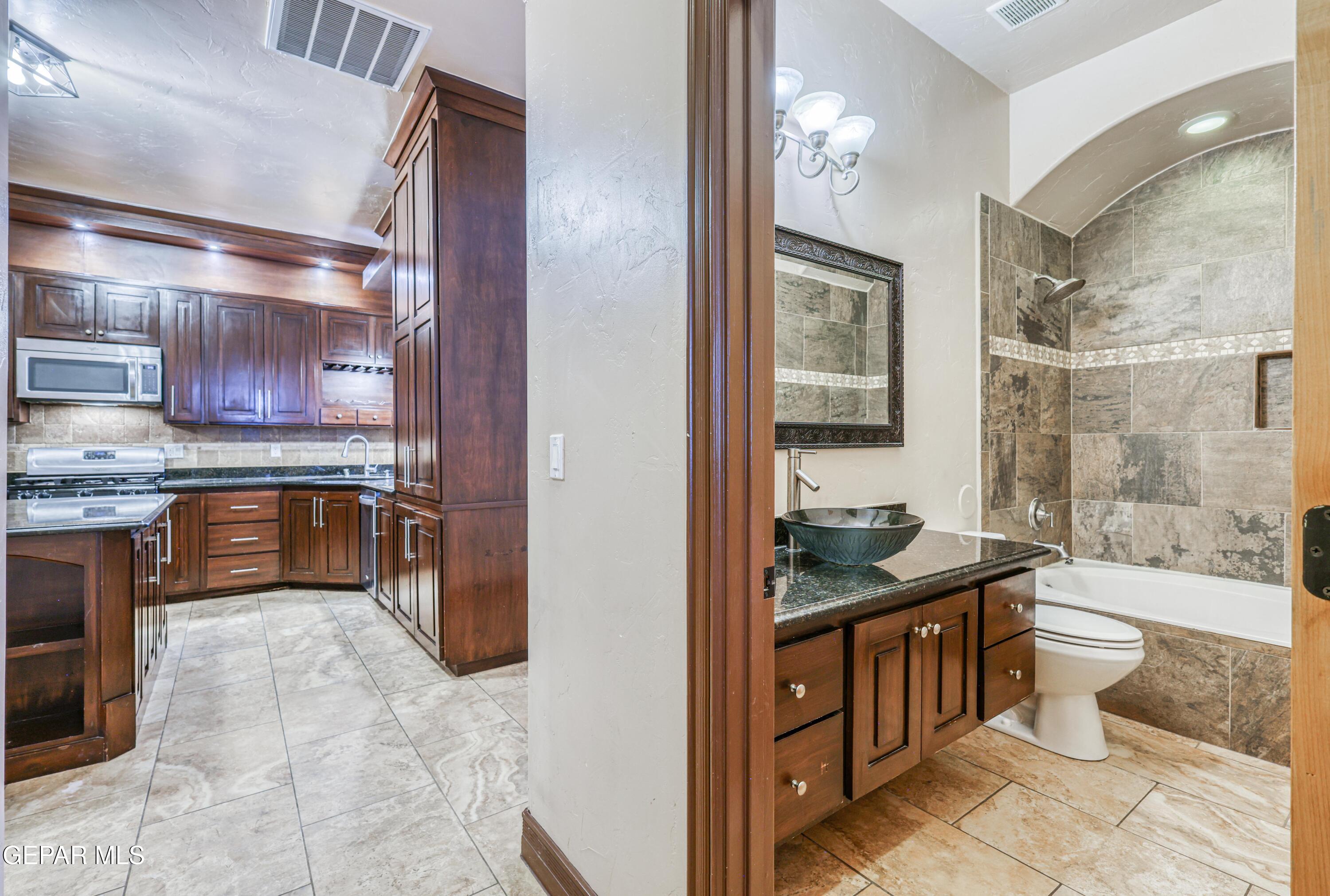 Kitchen with dark wood cabinetry beside a bathroom with a tiled tub and vessel sink.