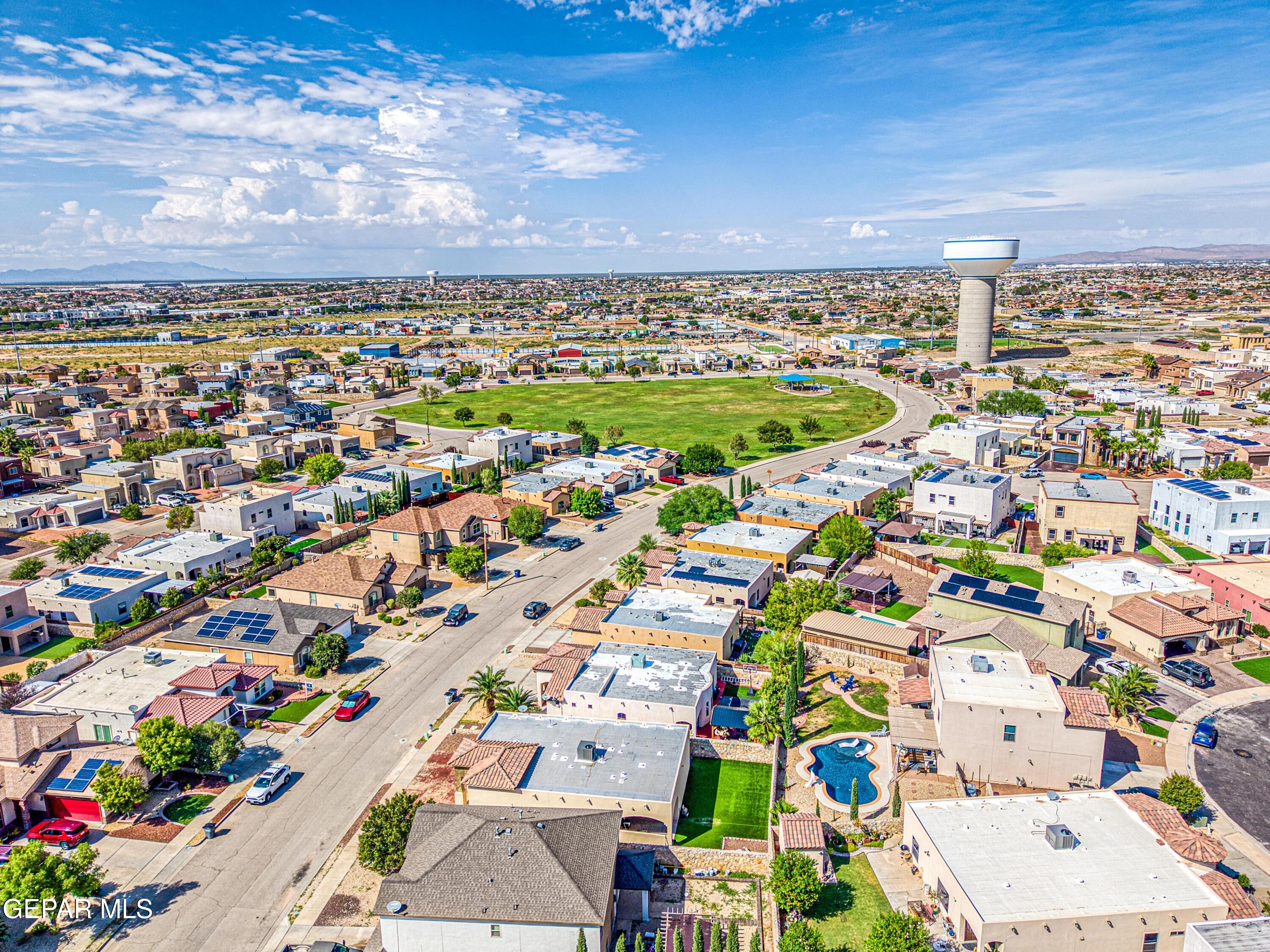 Aerial residential neighborhood surrounding a green park, water tower, and backyard pool.