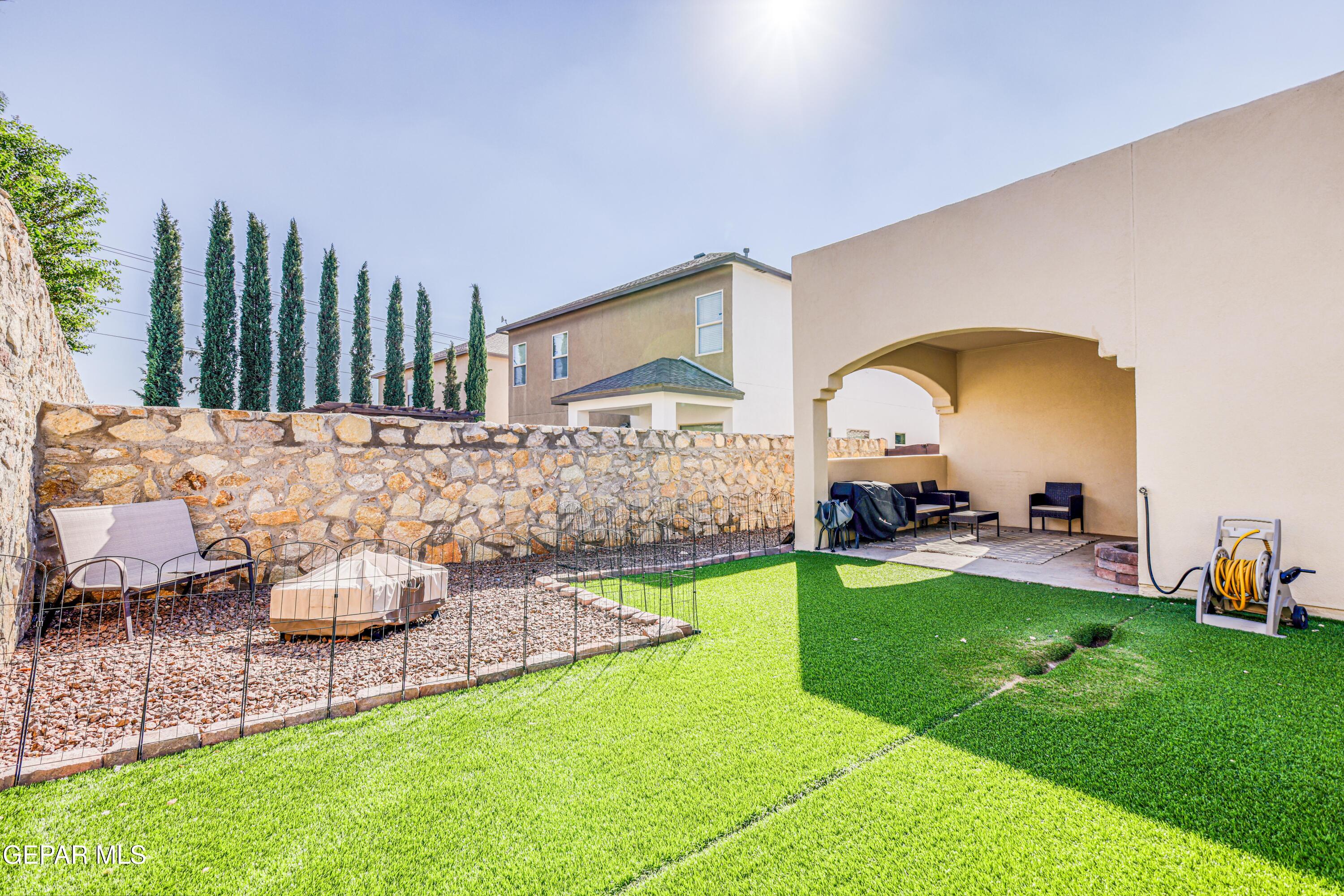 Backyard with a covered seating patio, bright green lawn, and stone-walled gravel garden.