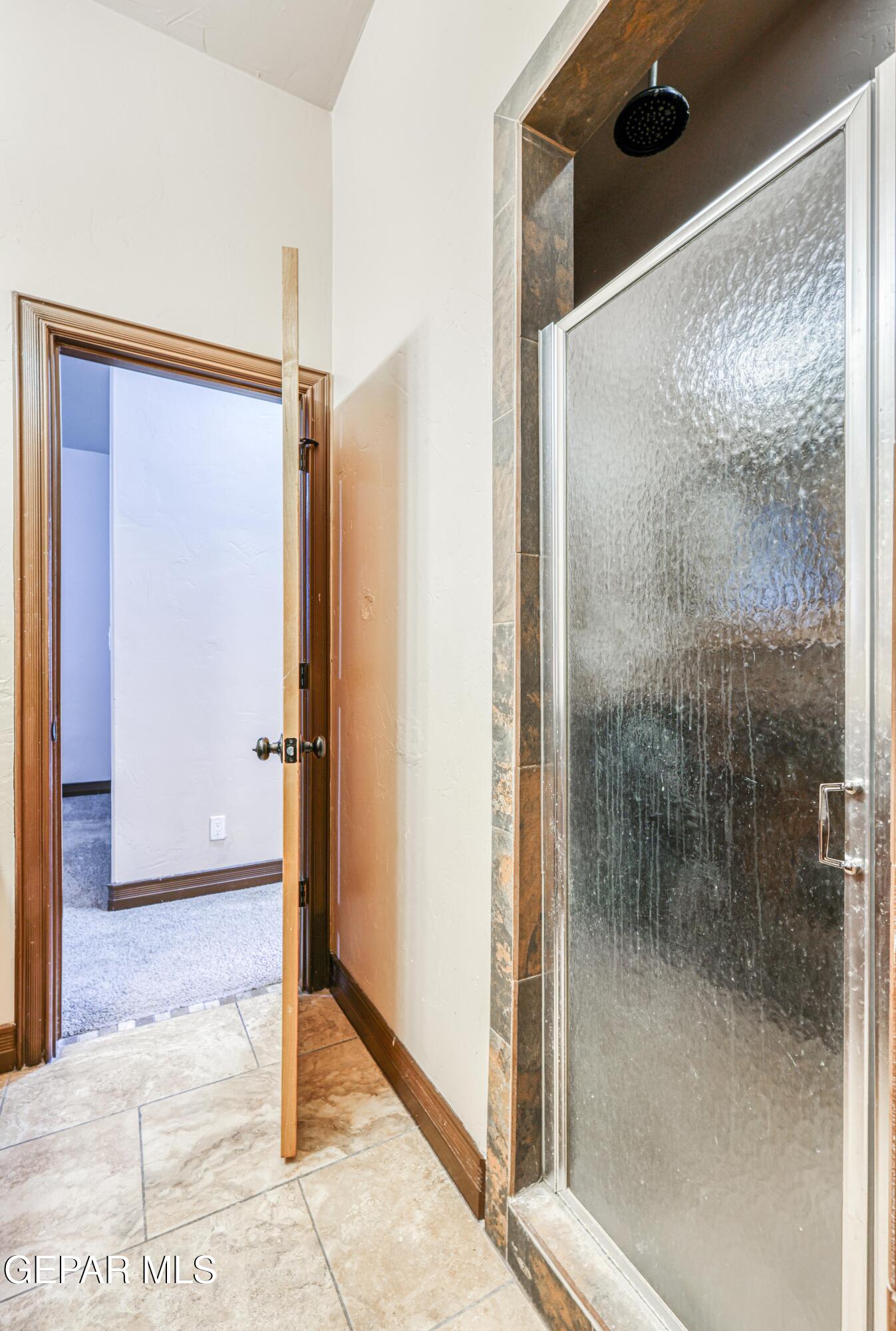 Bathroom shower with textured glass enclosure, dark rainfall showerhead, and stone-look tile surround.