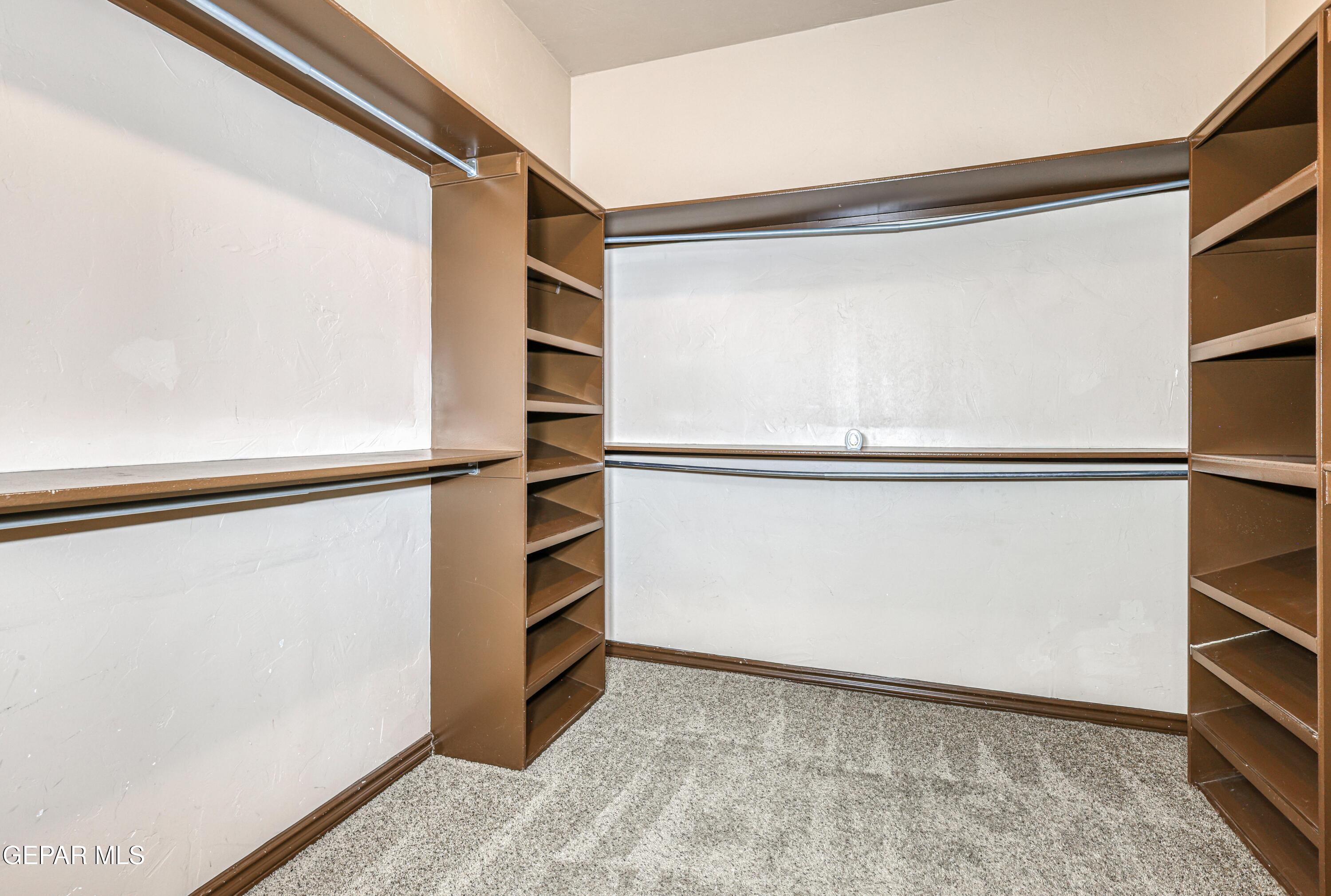Walk-in closet with brown built-in shelves, hanging rods, and gray carpet.