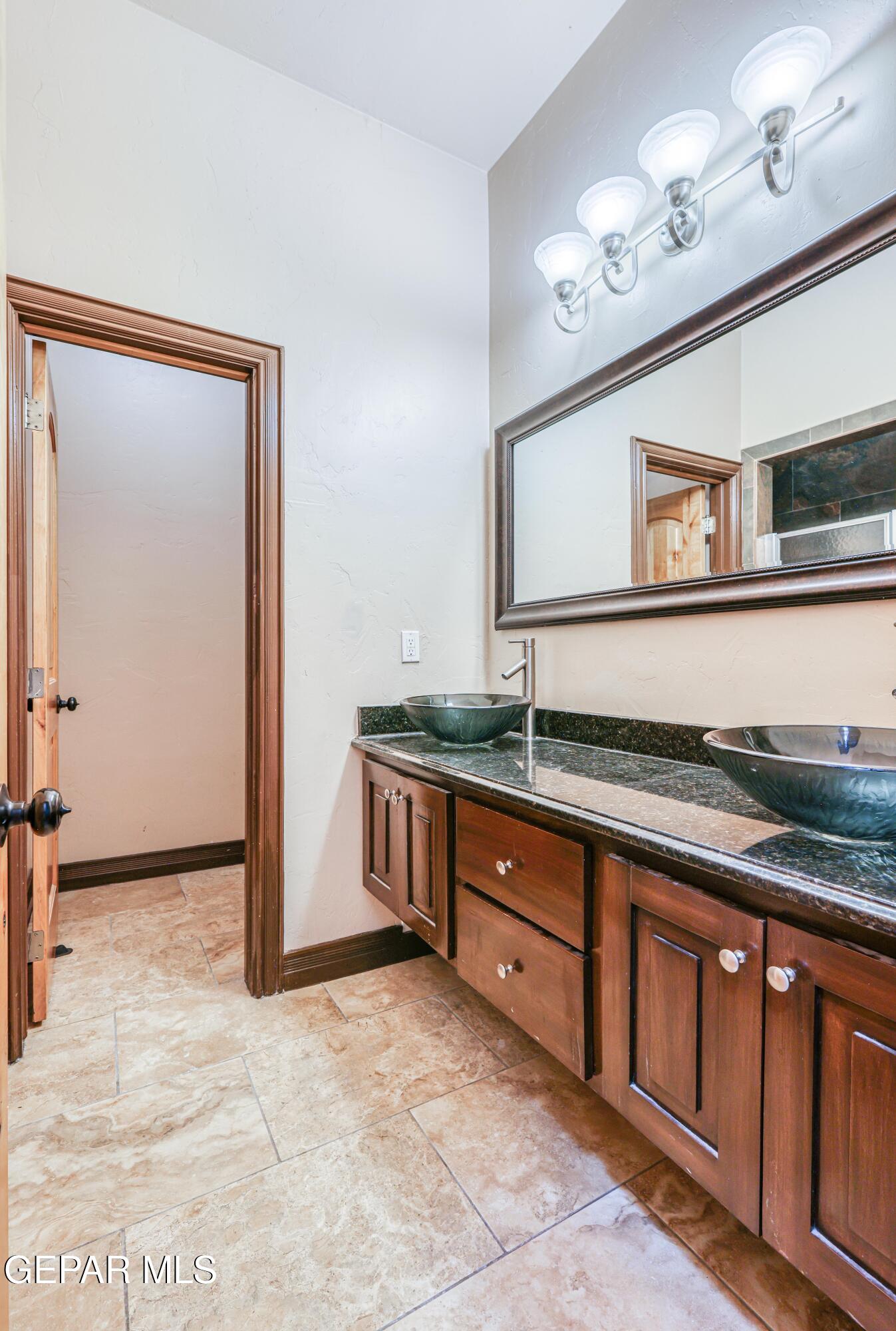 Bathroom with a dark granite double vanity, vessel sinks, wood cabinets, and a large framed mirror.
