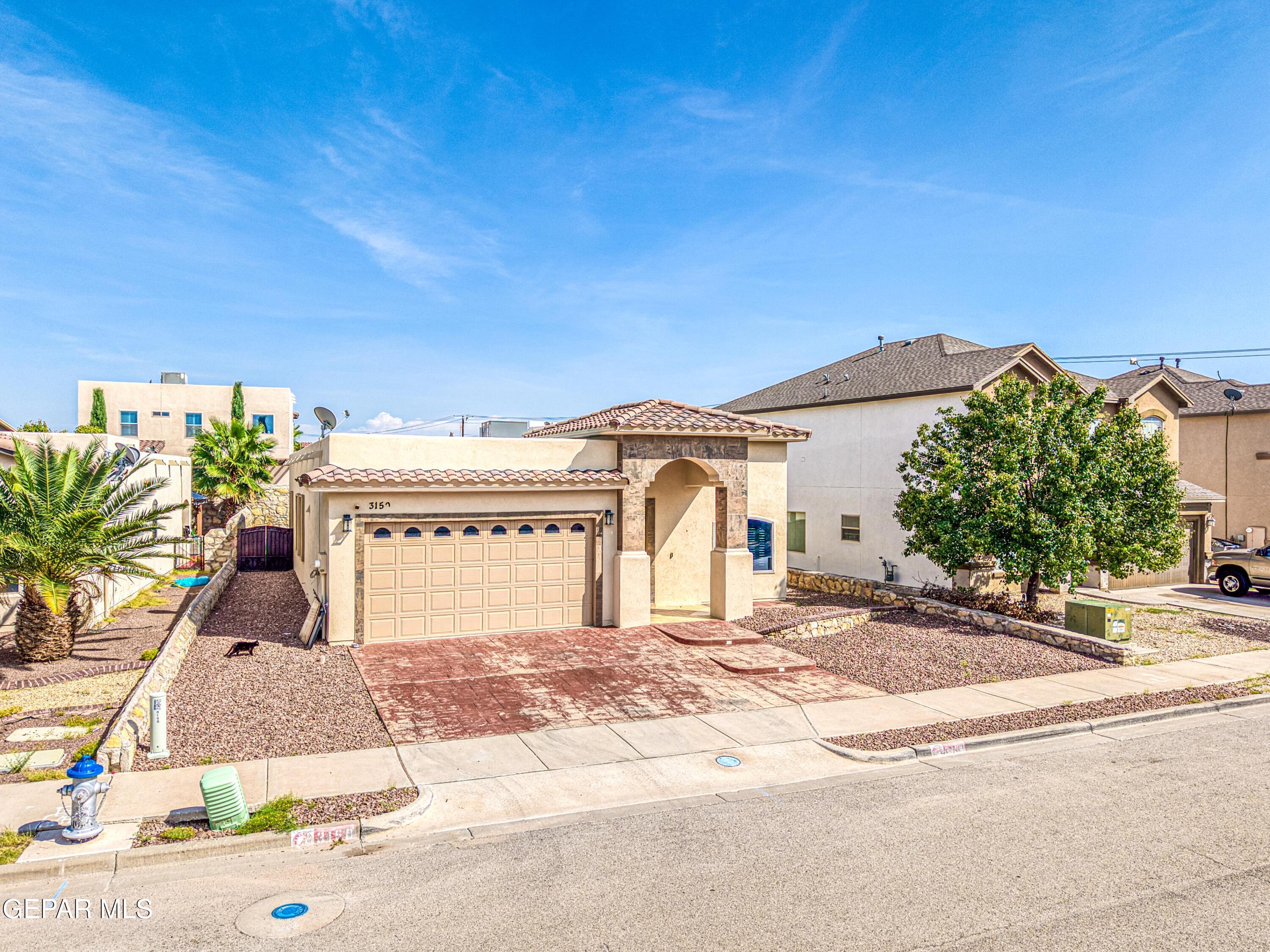 Tan stucco home with an arched entry, double garage, and gravel landscaping.