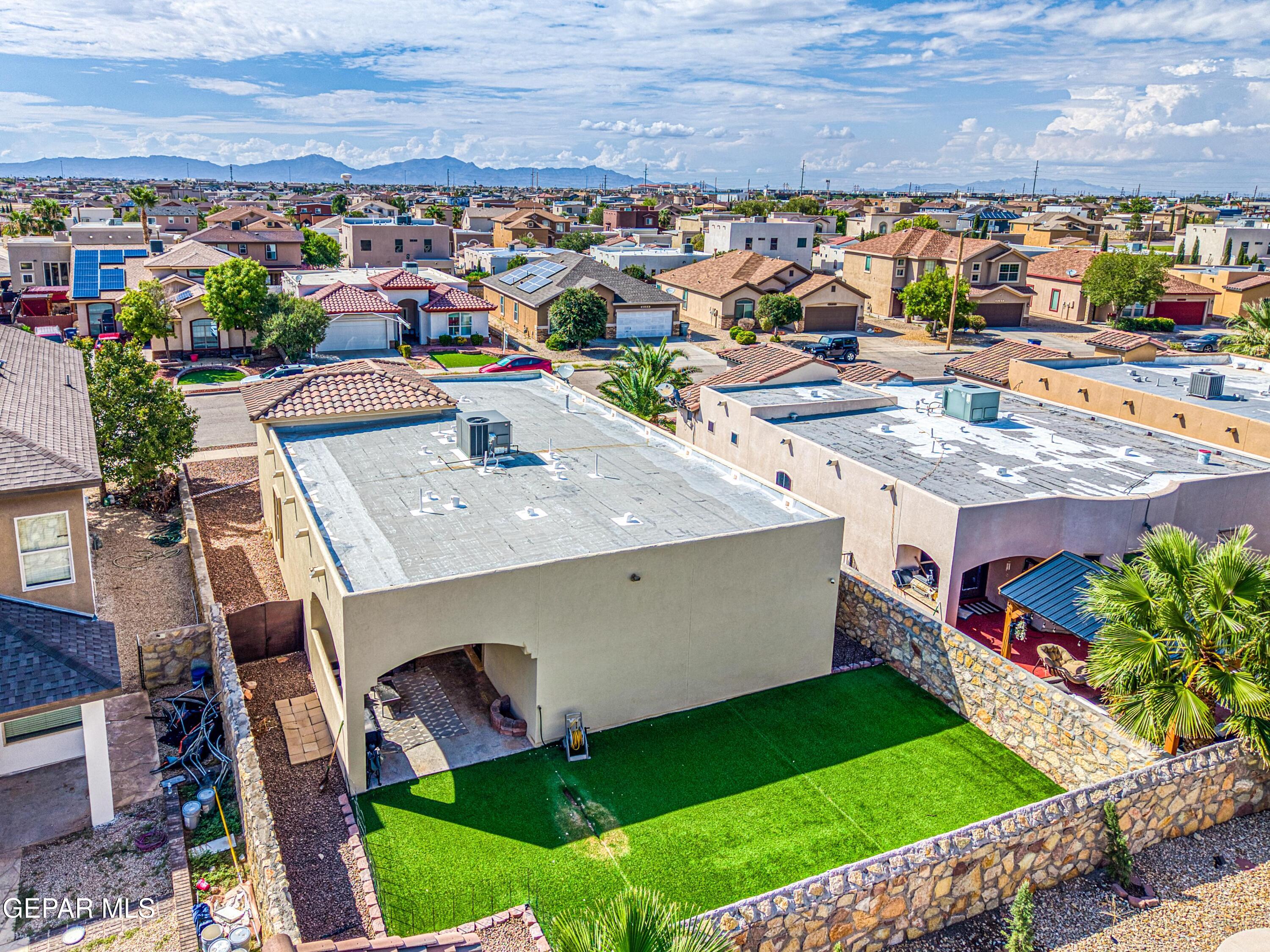 Aerial view of a walled backyard with artificial turf and mountains in the distance.
