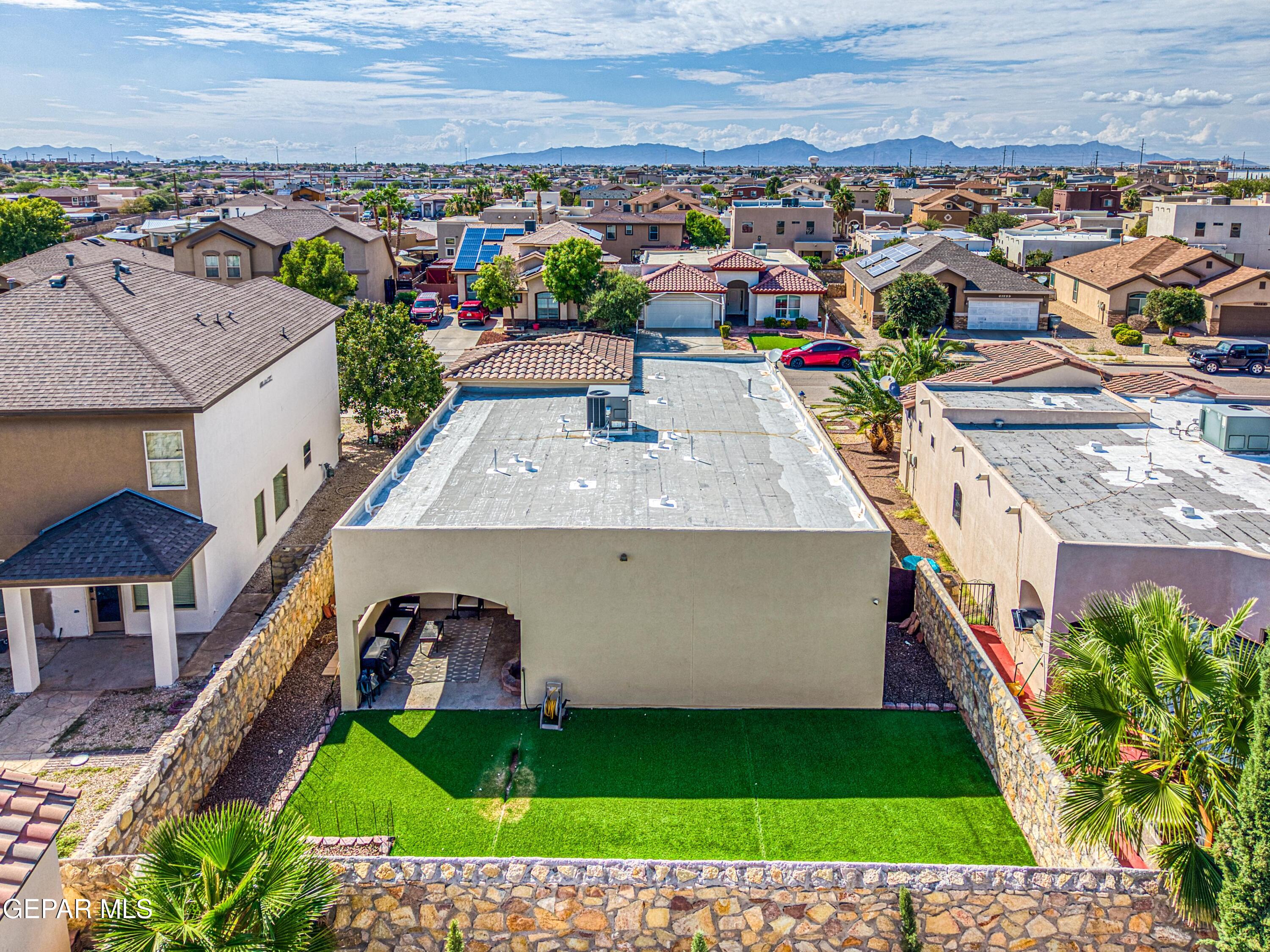Aerial view of a walled backyard with artificial turf, covered patio, and mountain views.