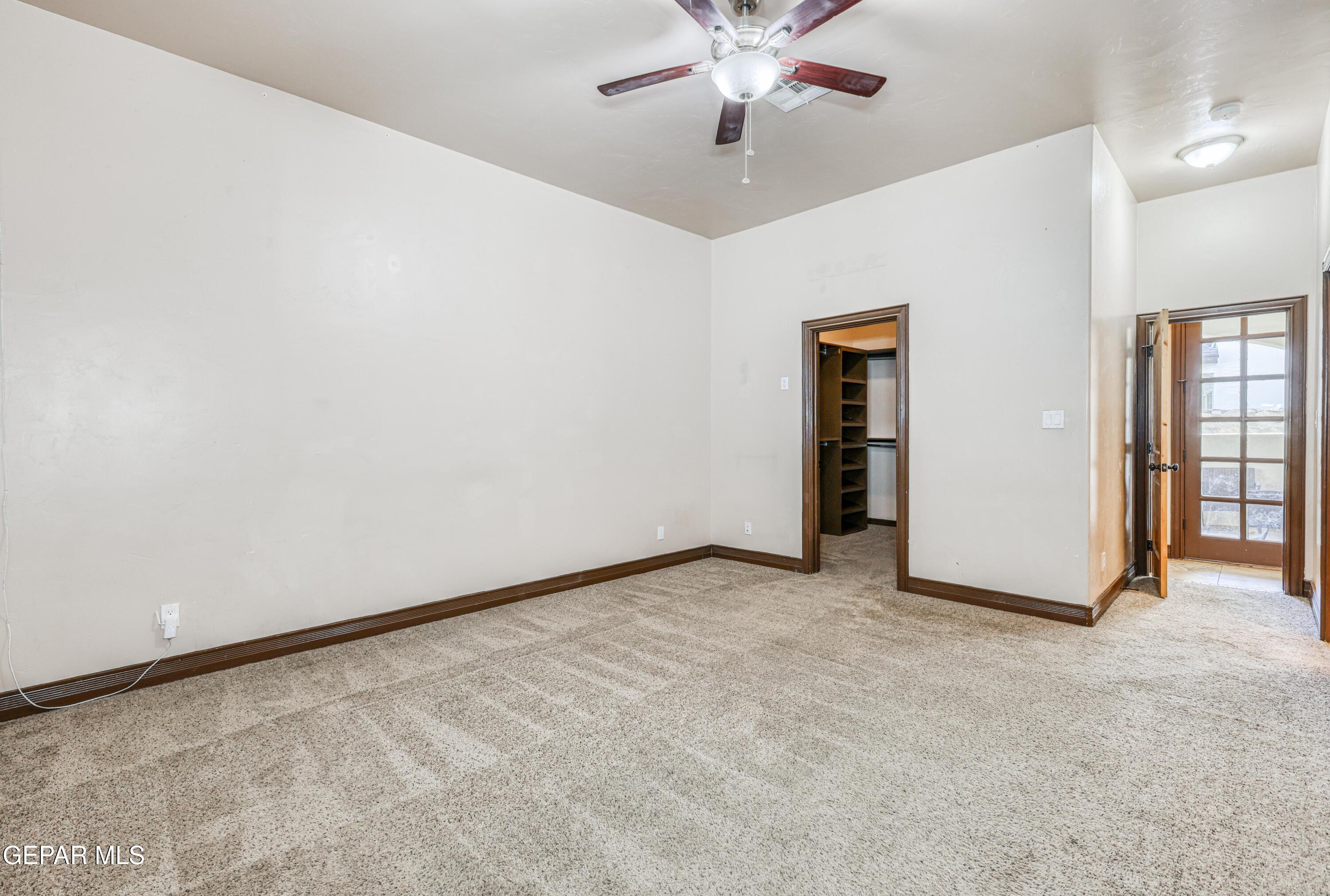 Empty carpeted bedroom with a ceiling fan, open walk-in closet, and glass-paneled exterior door.