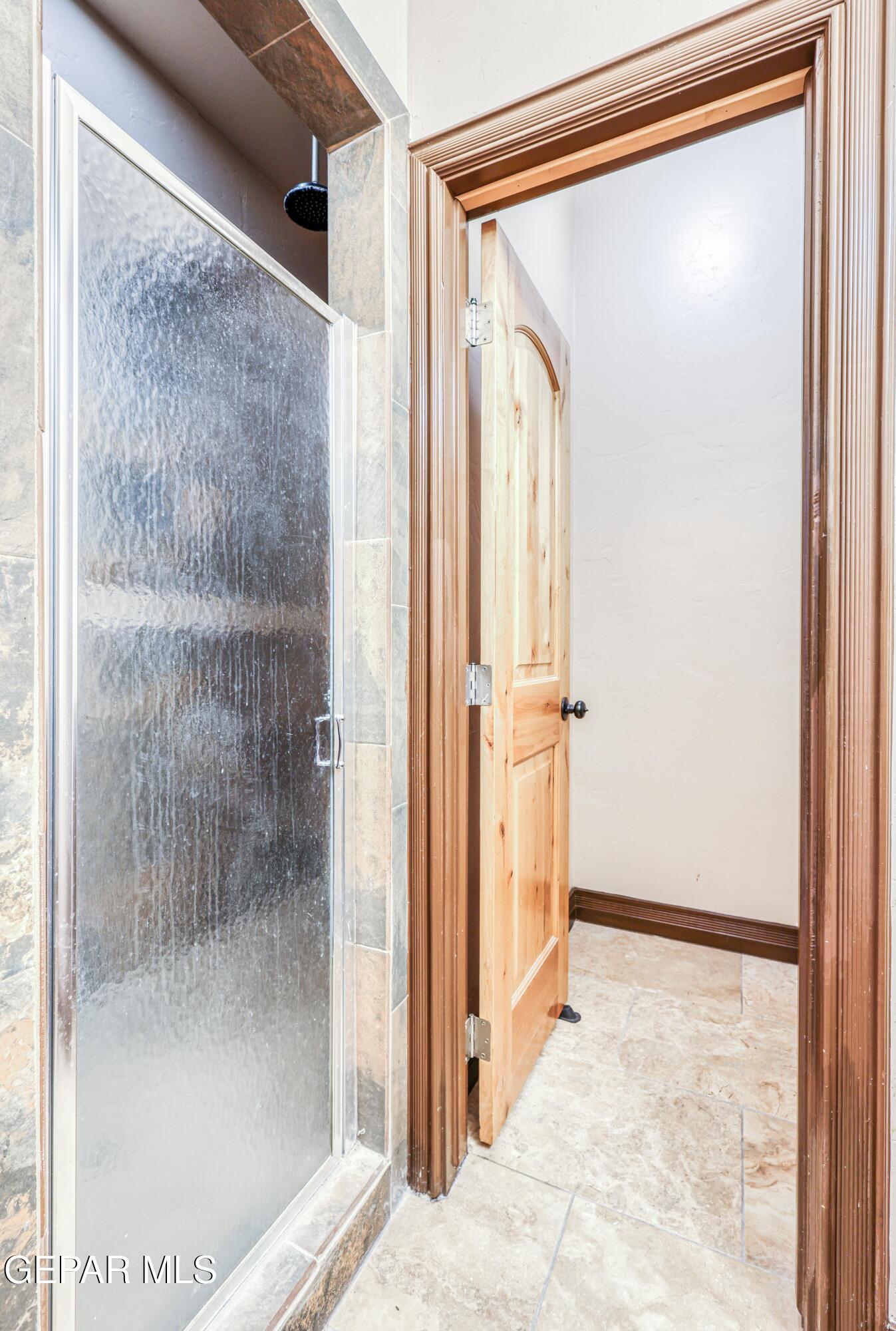 Bathroom shower with textured glass enclosure, tile surround, and open wood door.