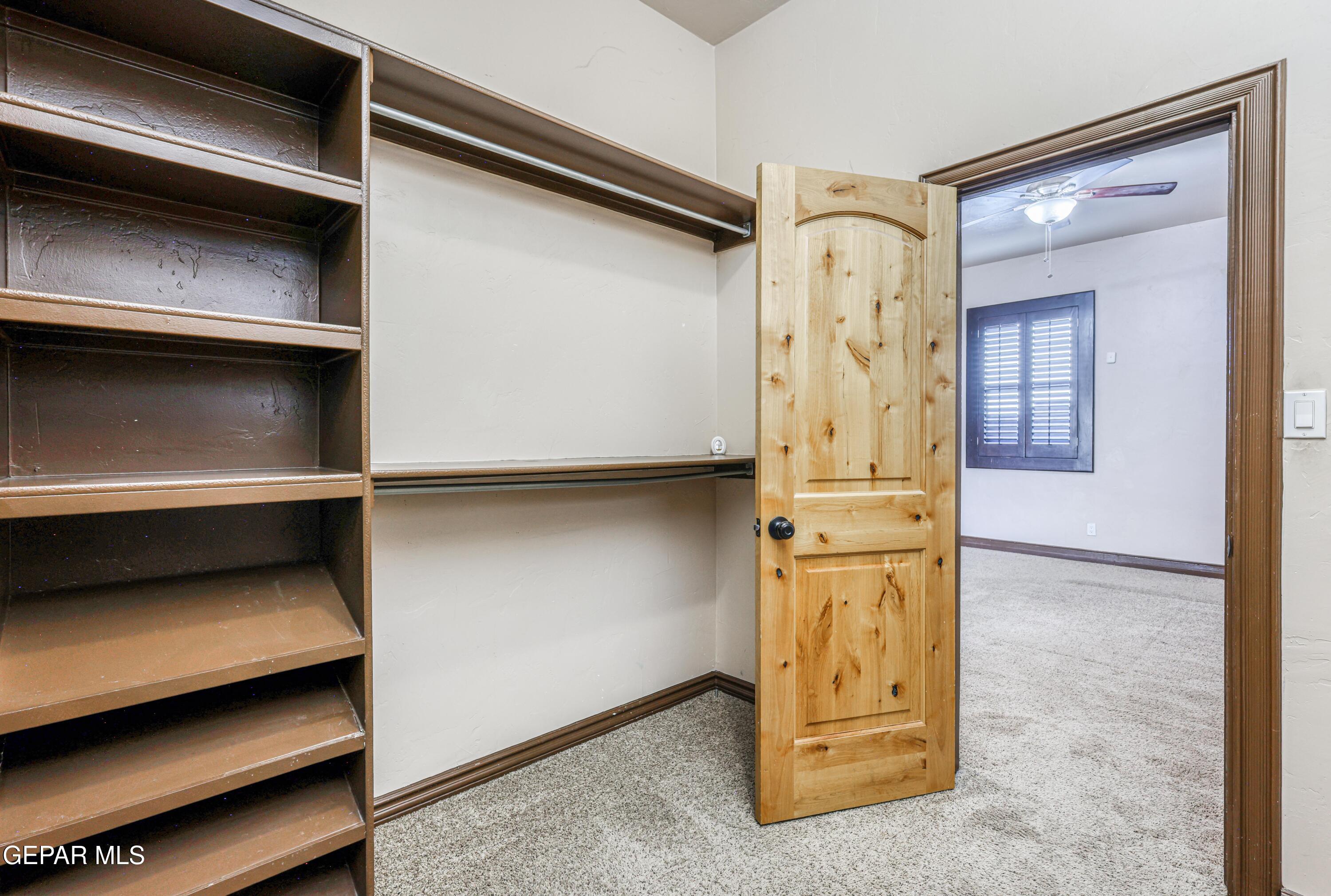 Walk-in closet with built-in shelving and hanging rod, opening to a carpeted bedroom through a wood door.