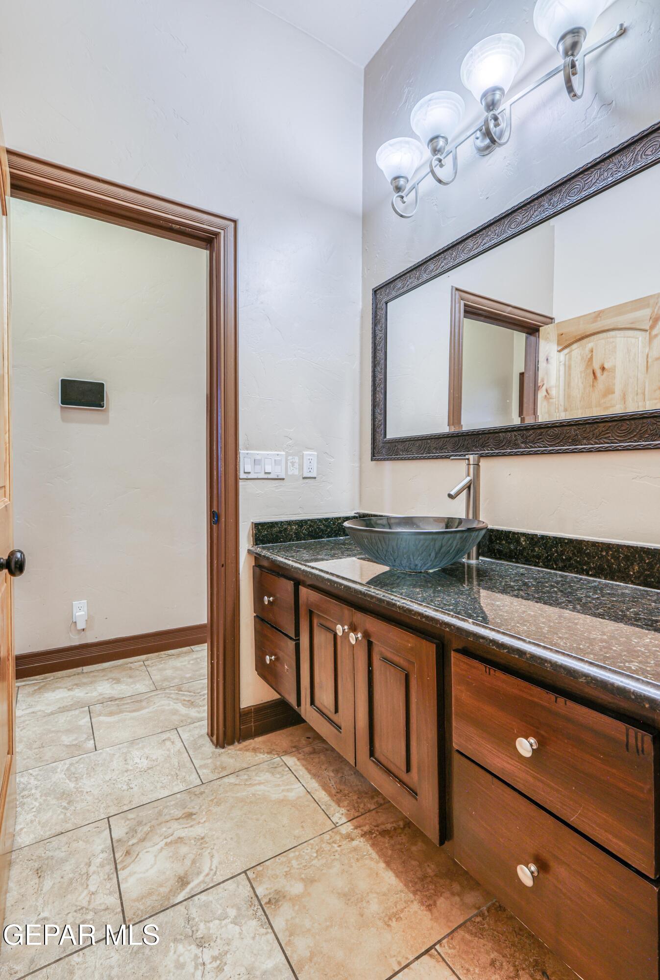 Bathroom vanity with a blue-gray vessel sink, dark granite countertop, and ornate framed mirror.