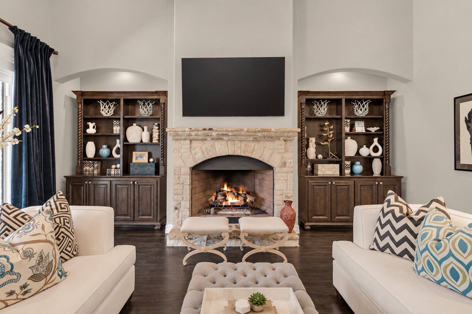 Living room with a stone fireplace, mounted television, matching built-ins, and white sofas.