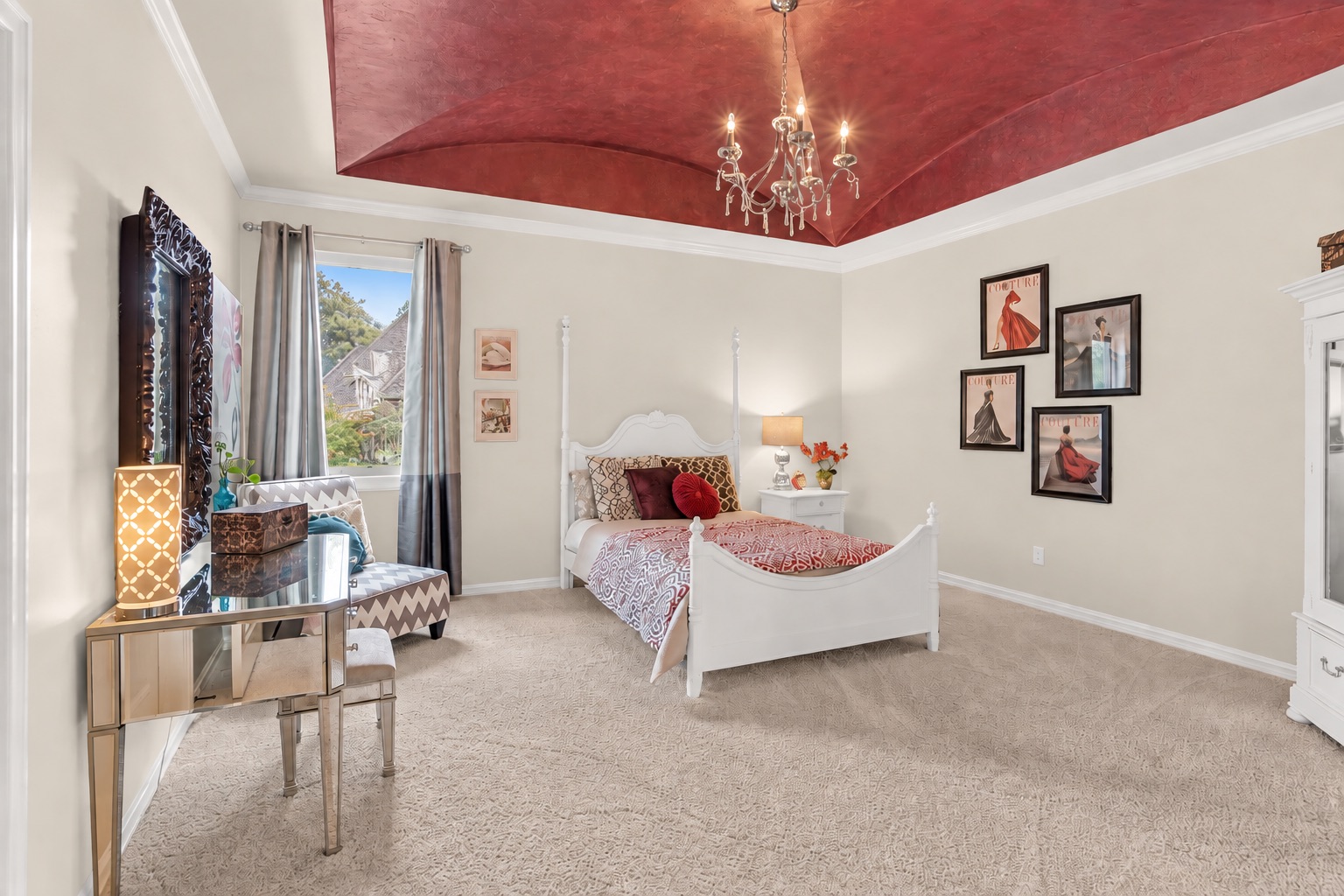 Bedroom with a white bed, dramatic red ceiling, chandelier, and fashion prints.