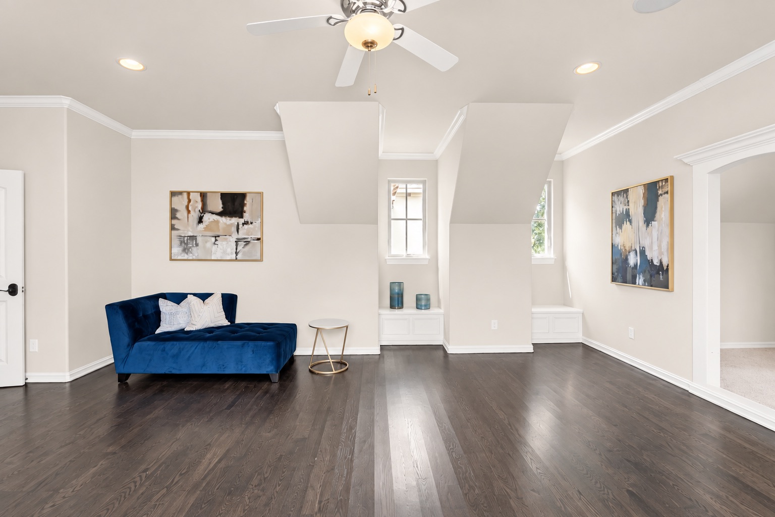 Bright sitting area with a blue chaise lounge, dark wood floors, and two narrow windows.
