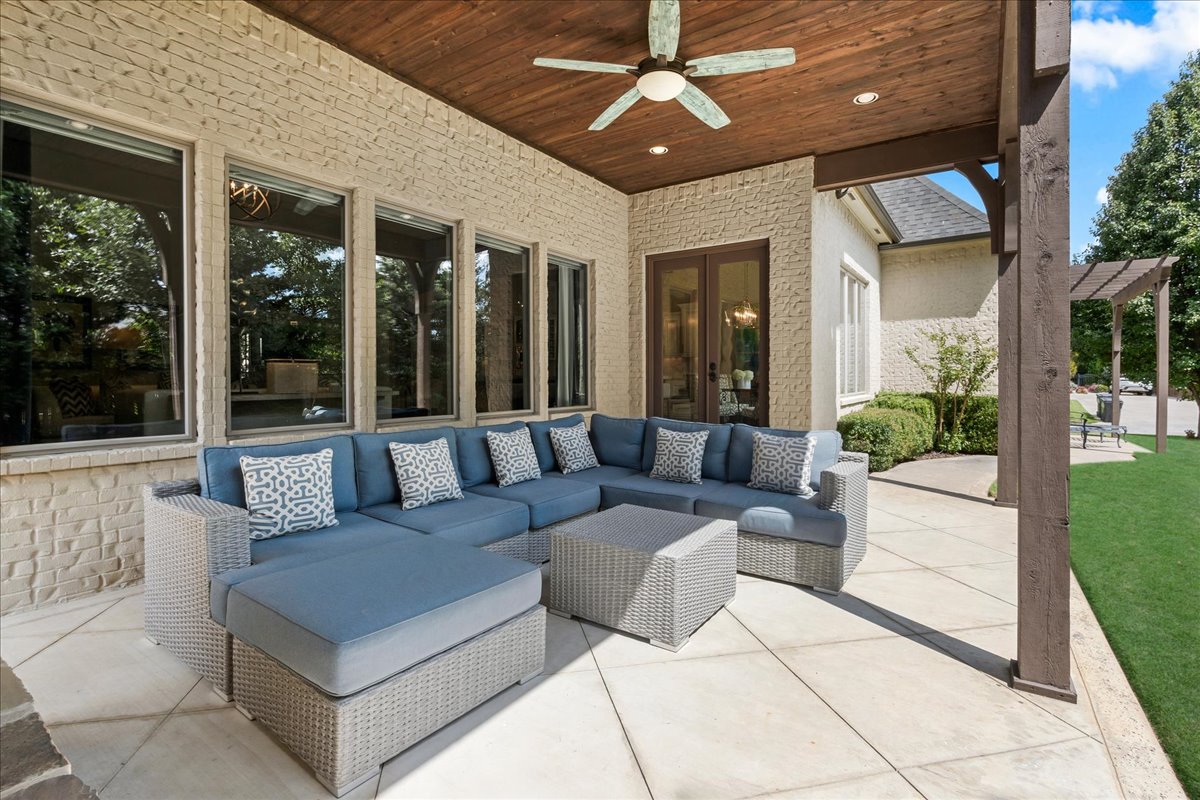 Covered patio with blue sectional seating, woven coffee table, and wood ceiling fan.