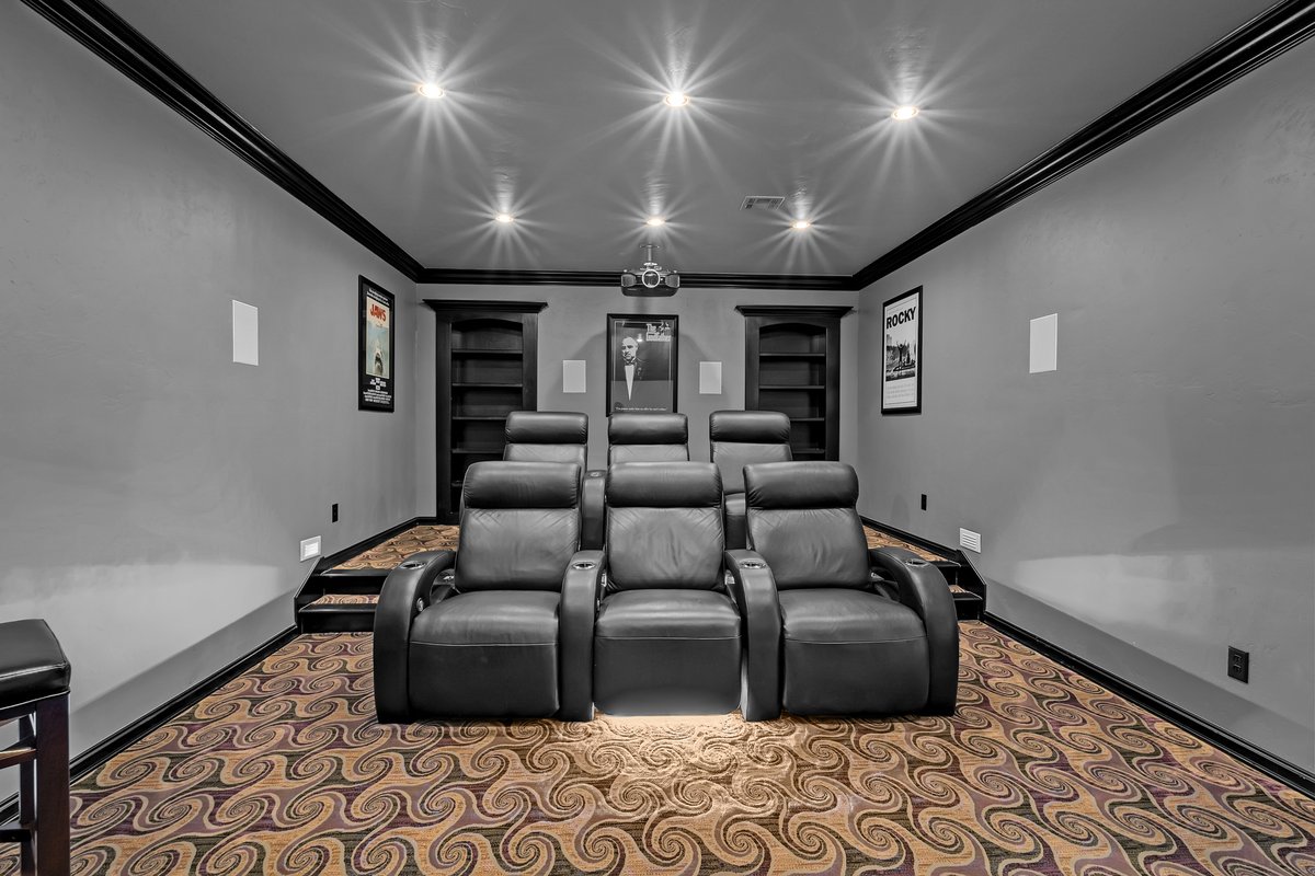 Home theater with black leather recliners, patterned carpet, built-in shelves, and recessed lighting.
