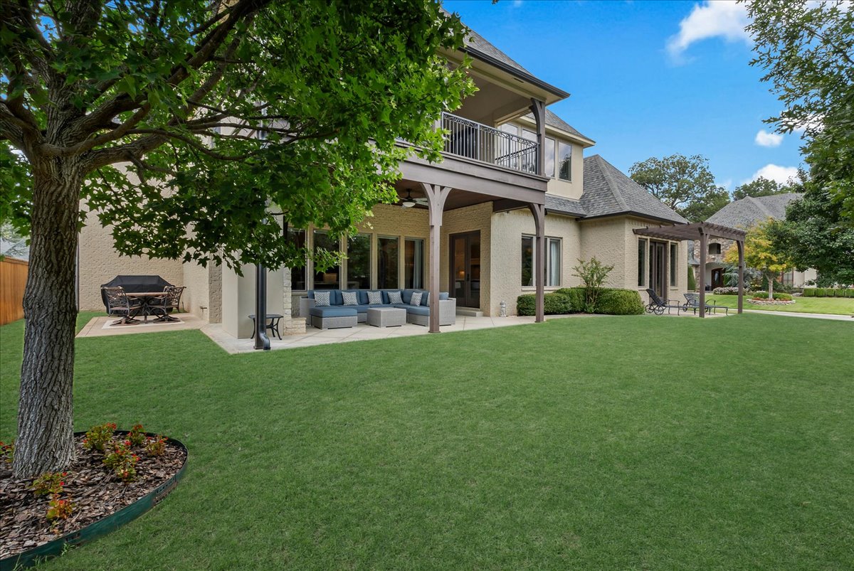 Two-story home's rear exterior with a covered patio, balcony, and spacious lawn.