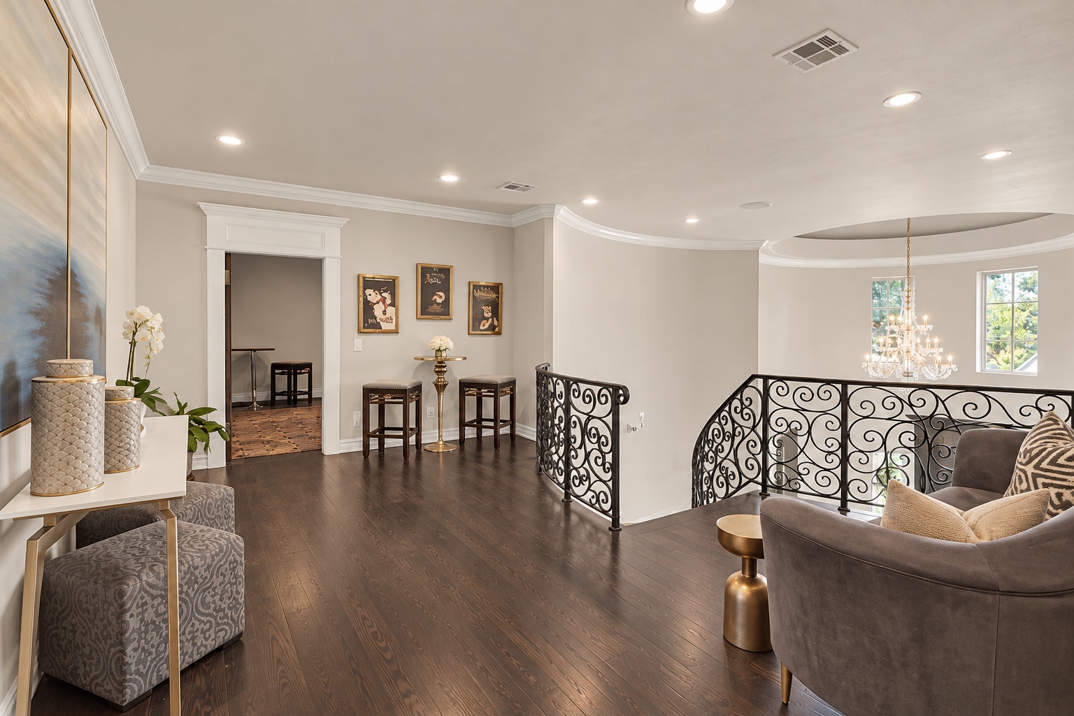 Upstairs sitting area with dark hardwood floors, an ornate iron stair railing, and chandelier.