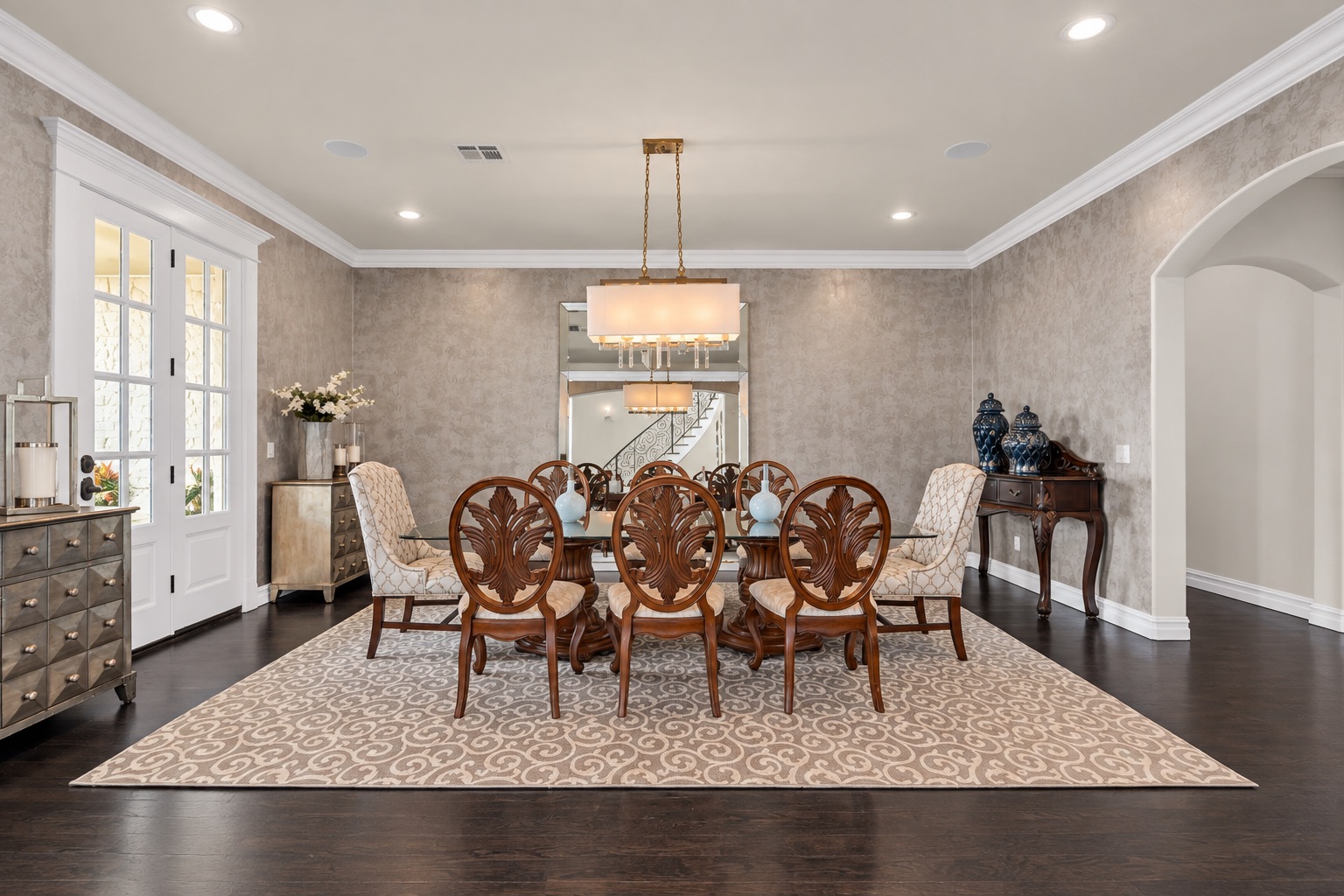 Dining room with carved wood furniture, patterned rug, chandelier, and French doors.