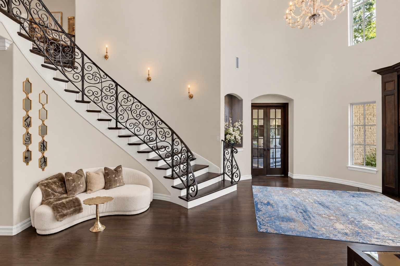 Double-height entry foyer with an ornate wrought-iron staircase, crystal chandelier, and blue patterned rug.