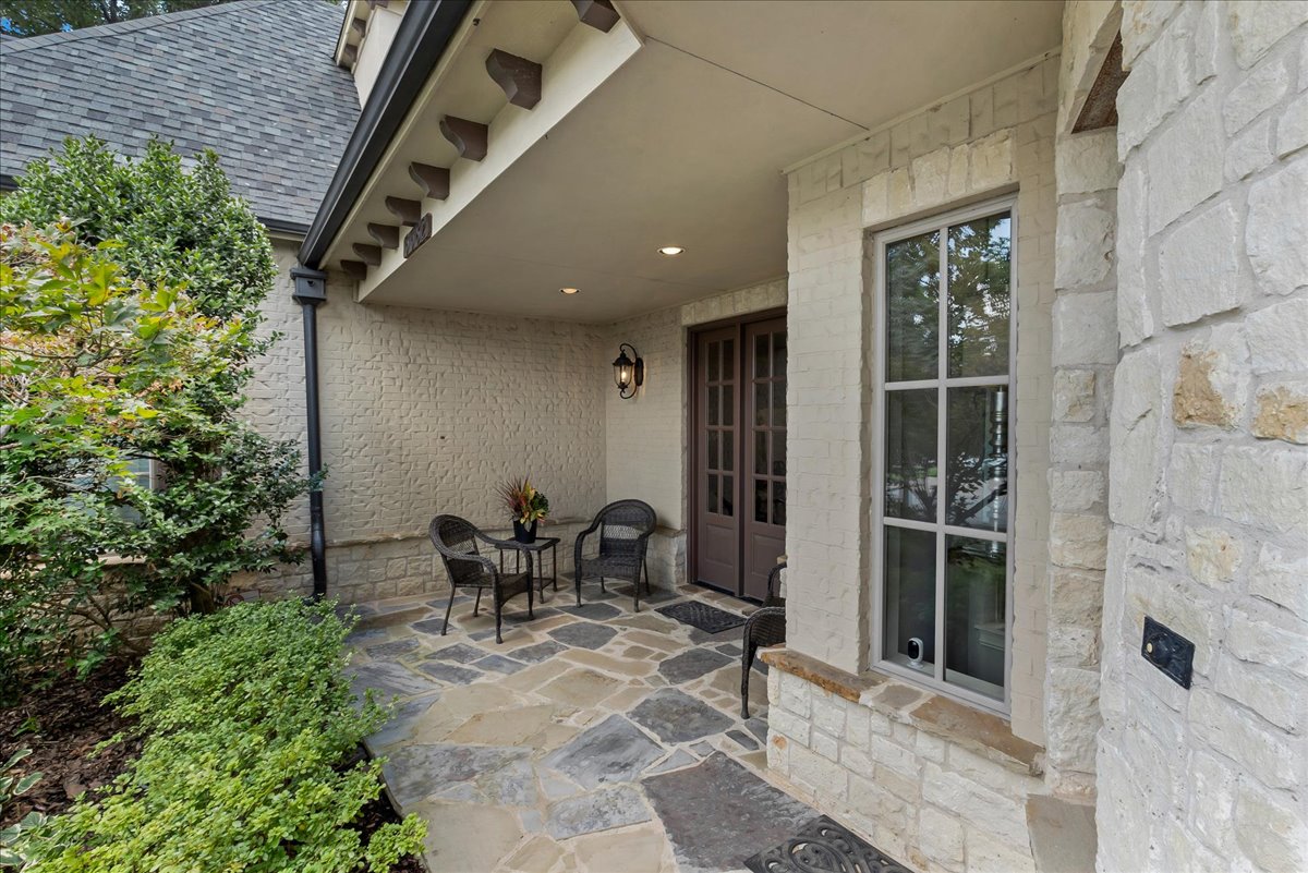 Covered front porch with stone paving, dark double doors, and a small outdoor seating area.