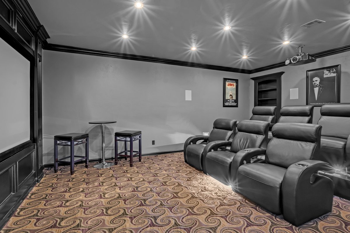 Home theater with black leather recliners, a ceiling-mounted projector, and movie posters.