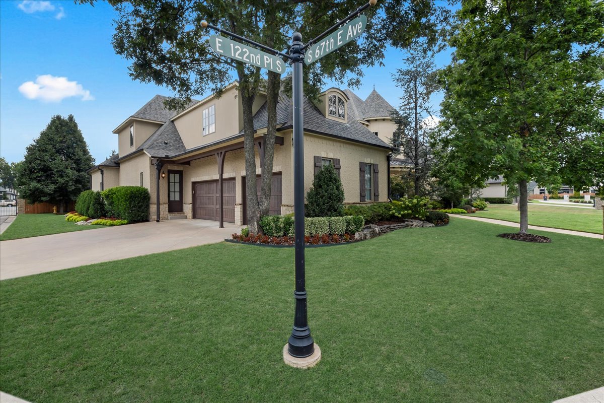 Beige two-story home with an attached garage and landscaped lawn, viewed from the corner street signs.