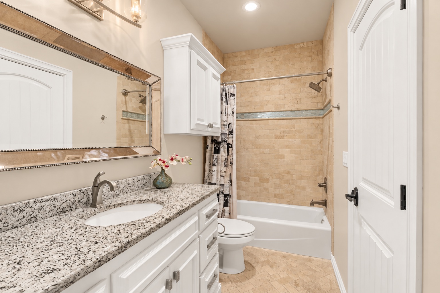 Bathroom with a granite vanity and tan-tiled tub-shower with a blue-green accent strip.
