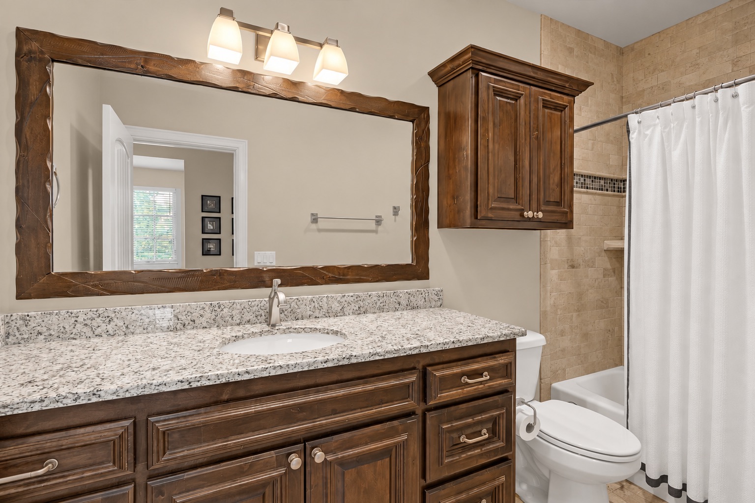 Bathroom with a dark wood vanity, speckled stone countertop, and tiled tub-shower.