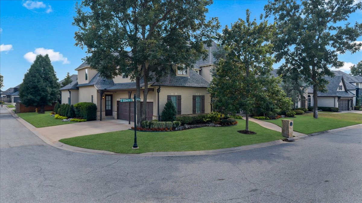 Two-story beige house on a landscaped corner lot beneath mature trees.