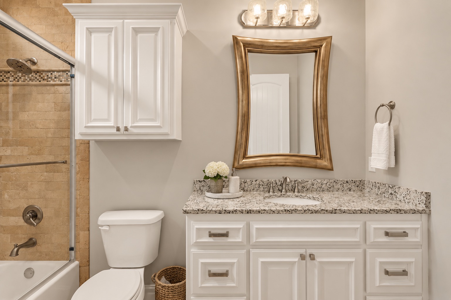 Bathroom with tan stone shower, white vanity, speckled granite counter, and framed mirror.